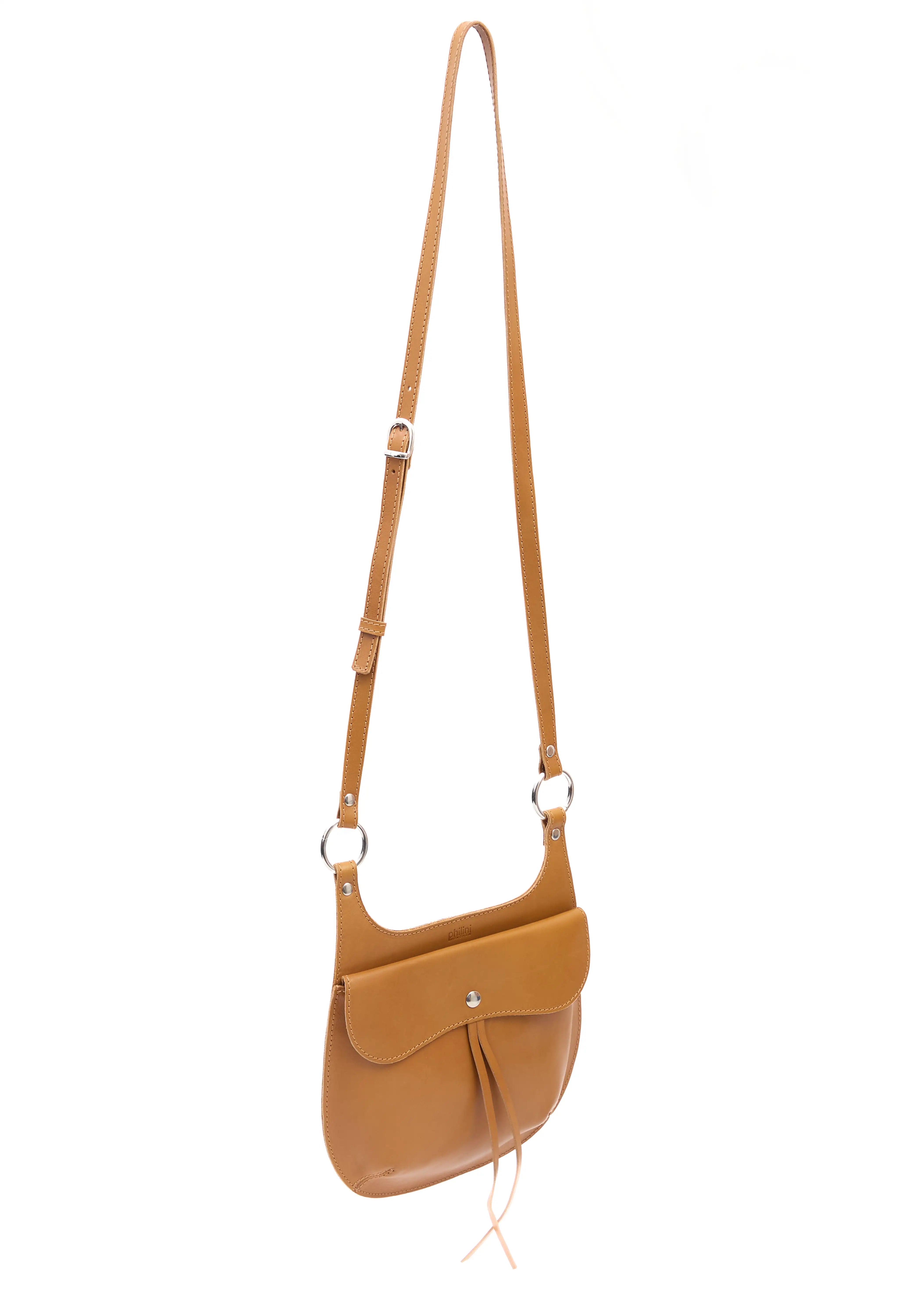 Side view of the Philini Cowboy Crossbody Bag in cognac calf leather, curved shape with front flap and snap button, long adjustable strap. Timeless crossbody in rich natural leather
