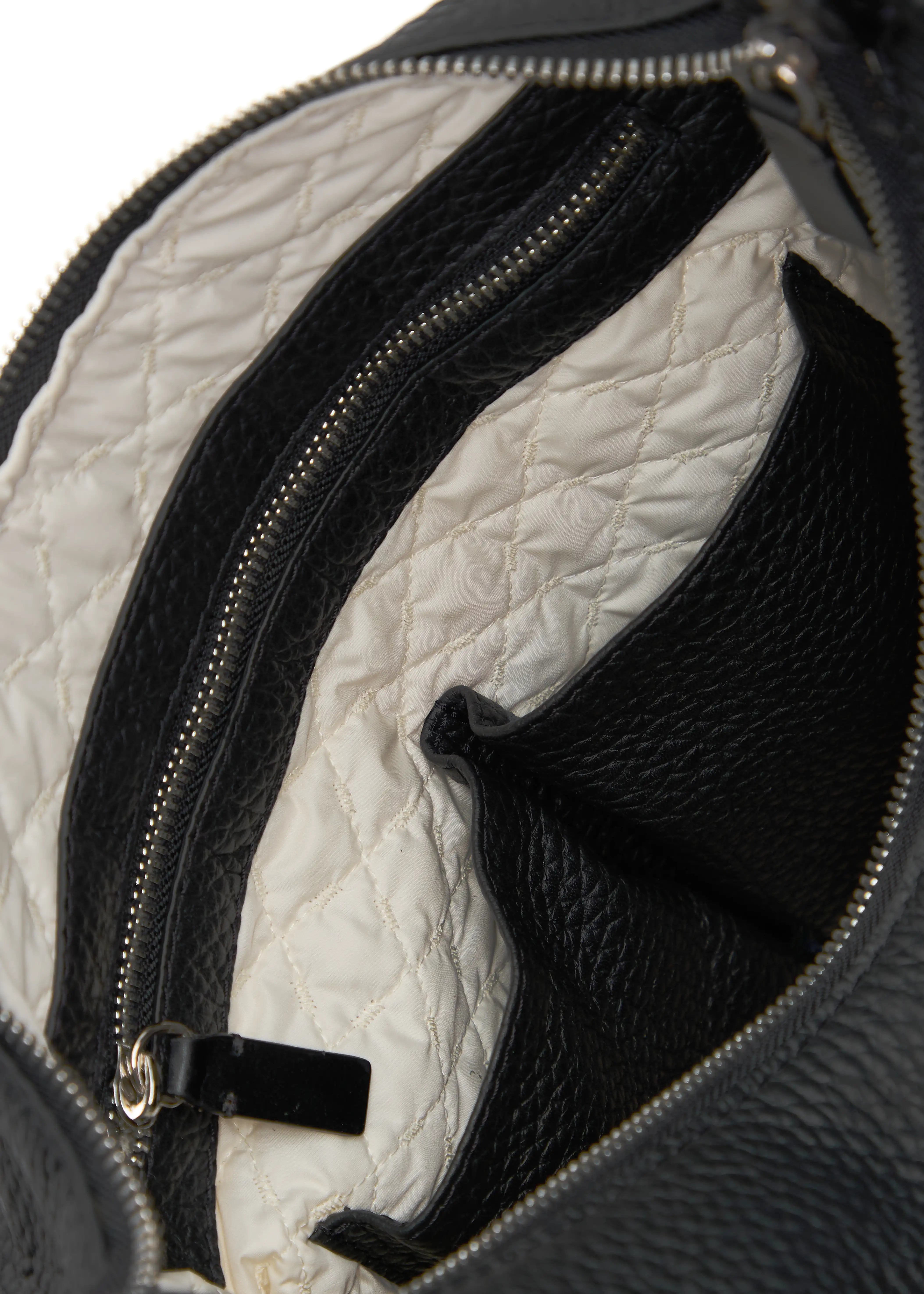 Interior view of the Philini Yana Black Leather Hobo Bag, featuring a vanilla-colored patterned lining, divided open pockets, a zippered pocket with leather trim, and a metal zipper closure. A handcrafted, eco-friendly luxury leather bag
