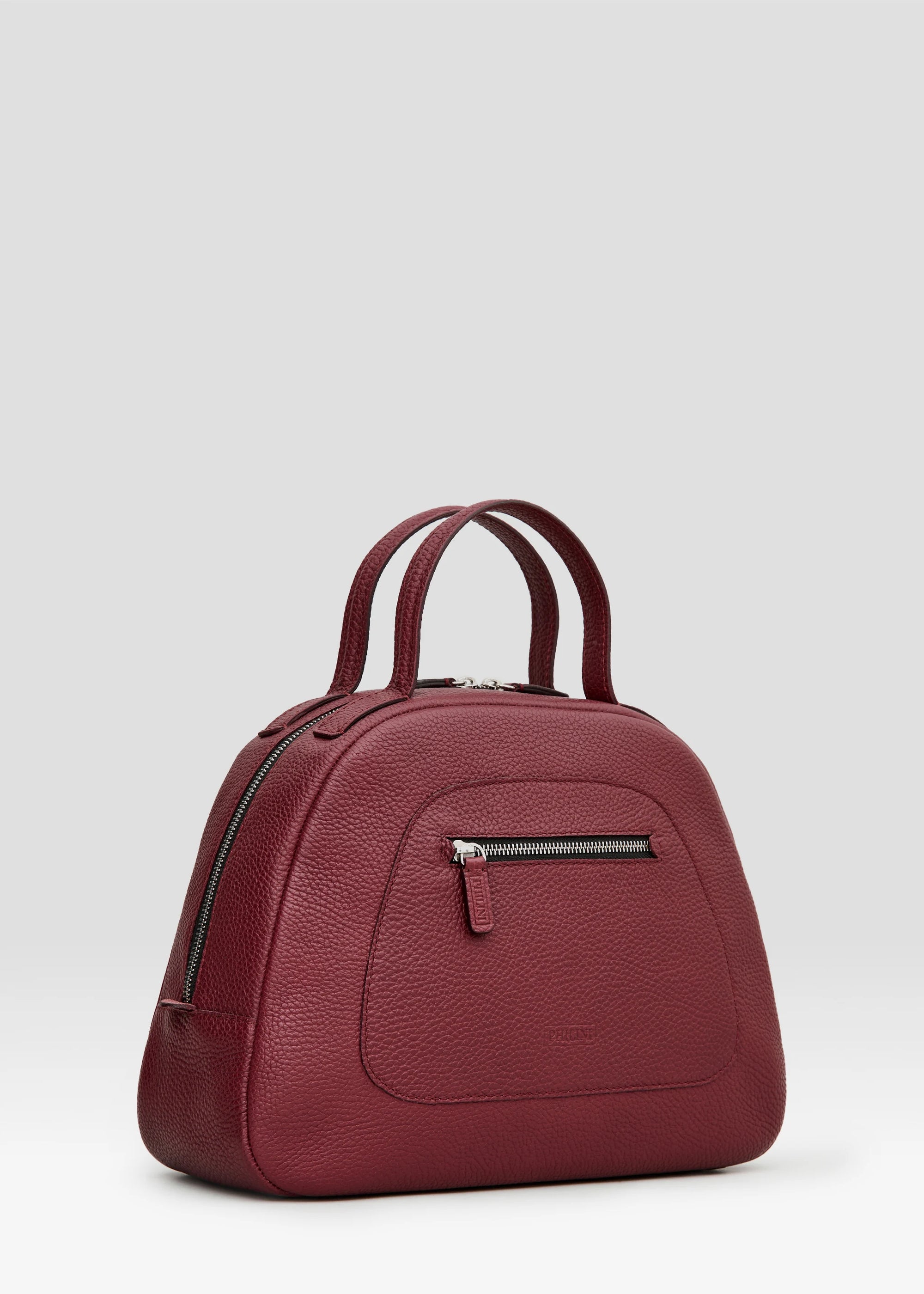 Side view of the Philini Domi Handbag in red calf leather, showcasing the dome shape, short handles, silver rivets, front zip pocket, and zipper closure. The elegant, premium accessory for timeless style. 