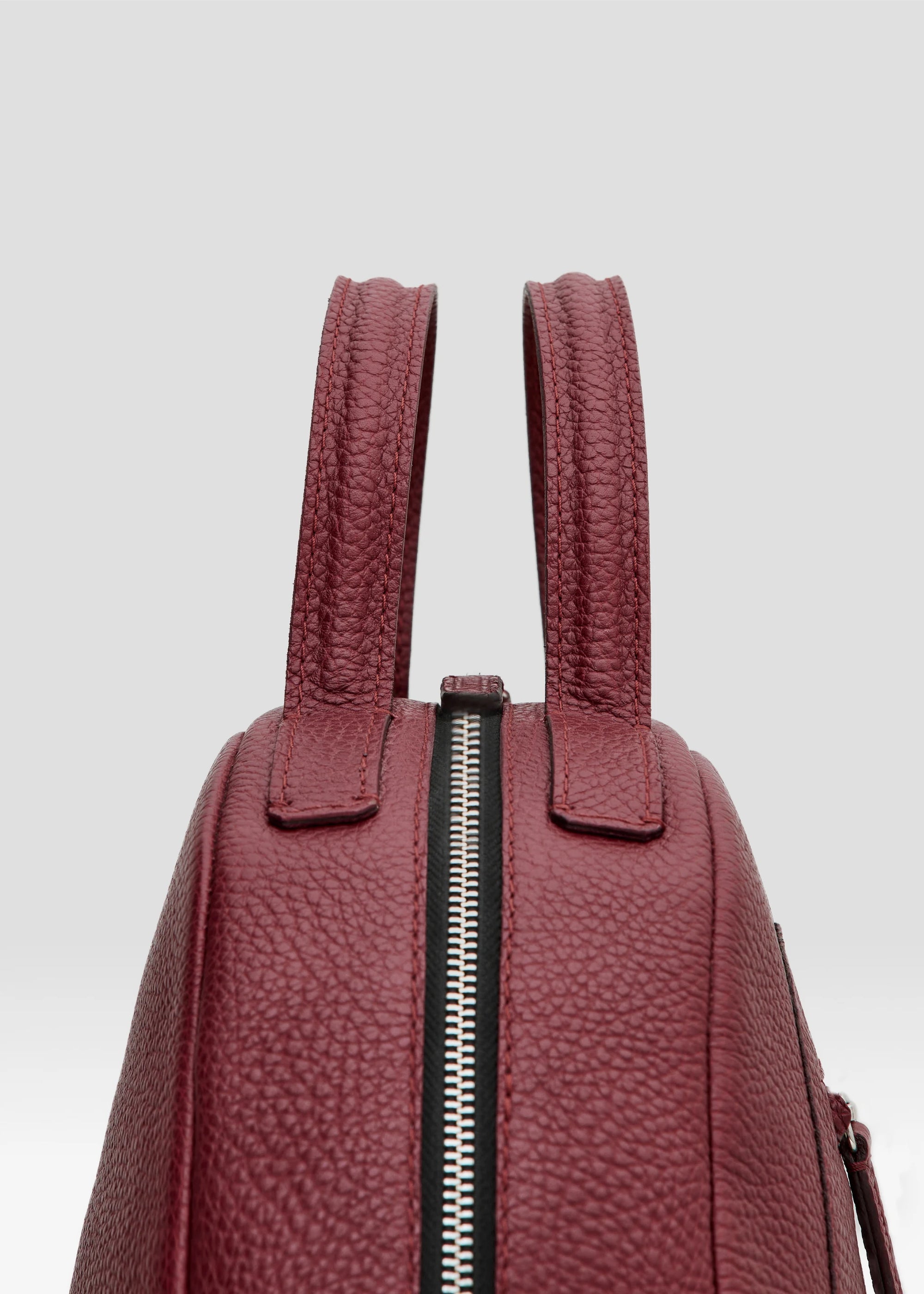 Detailed view of the Philini Domi red Handbag in dome shape, handcrafted from calf leather and finished with short leather handles, silver rivets, and a zipper closure. The interior features a vanilla-colored lining and zippered inner pockets.