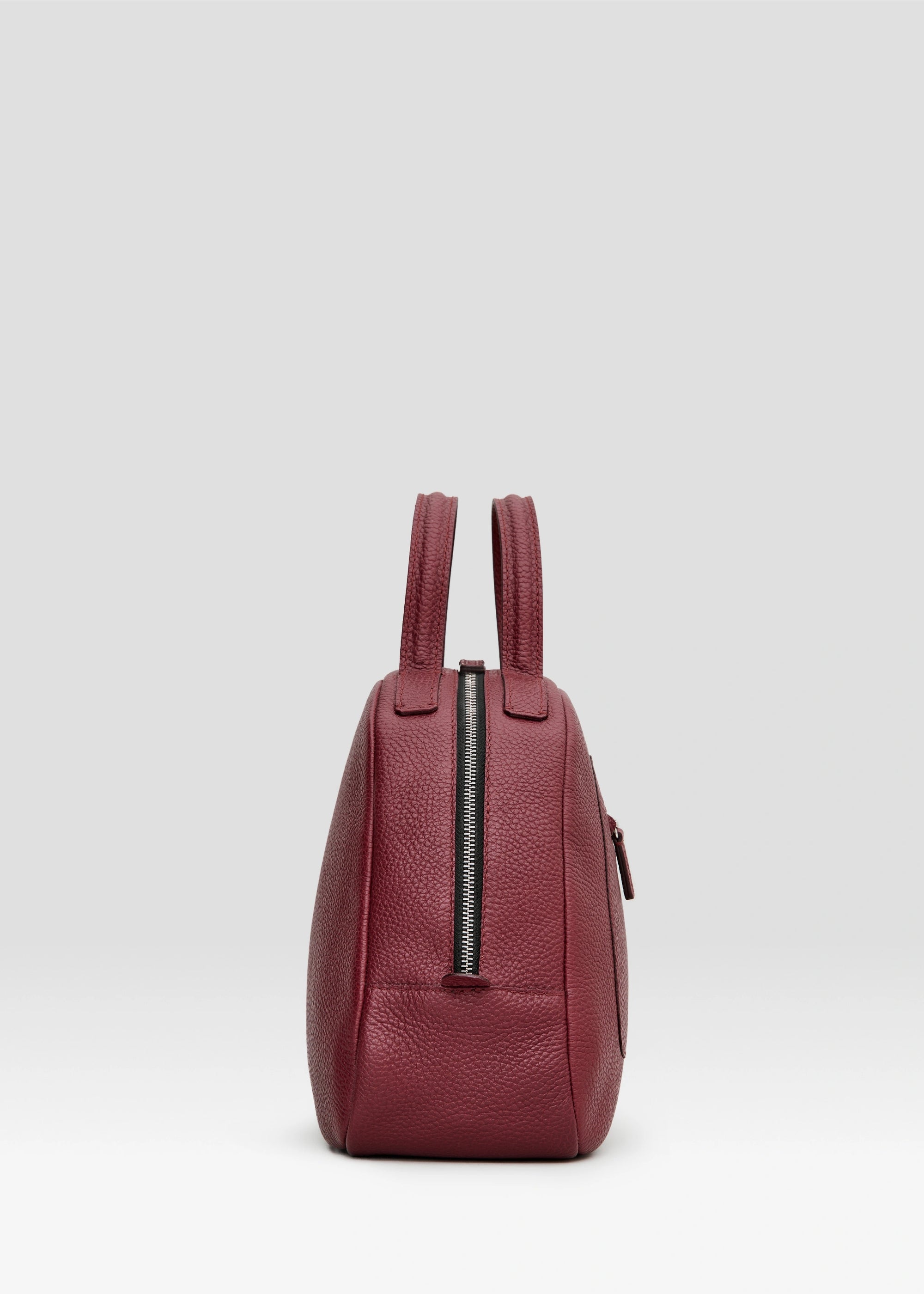 Profile view of the Philini Domi Handbag in red calf leather, showcasing the dome shape, short handles, silver rivets, front zip pocket, and zipper closure. The elegant, premium accessory for timeless style. 