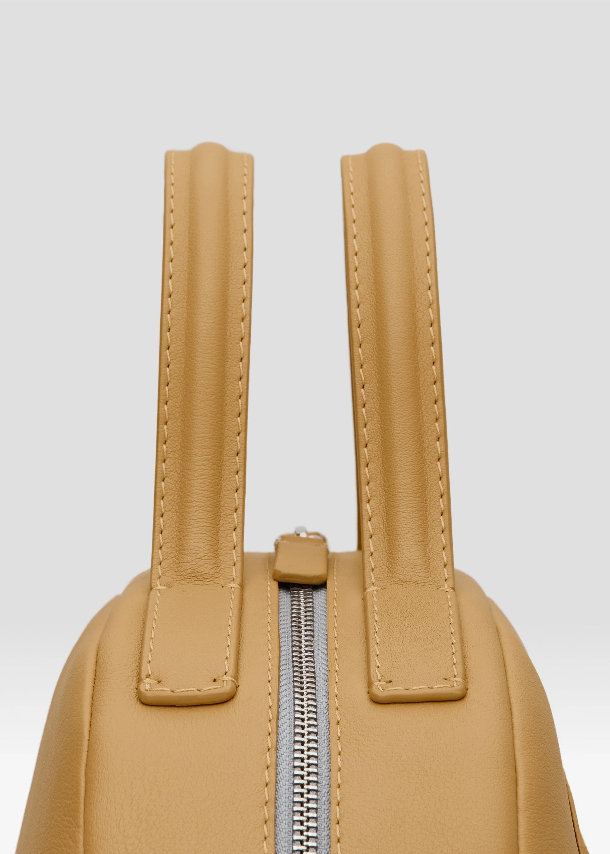Detailed view of the yellow Philini Domi Handbag in soft nappa leather, showing dome shape, short handles, front zip pocket, and silver hardware. A stylish and handcrafted everyday leather bag 