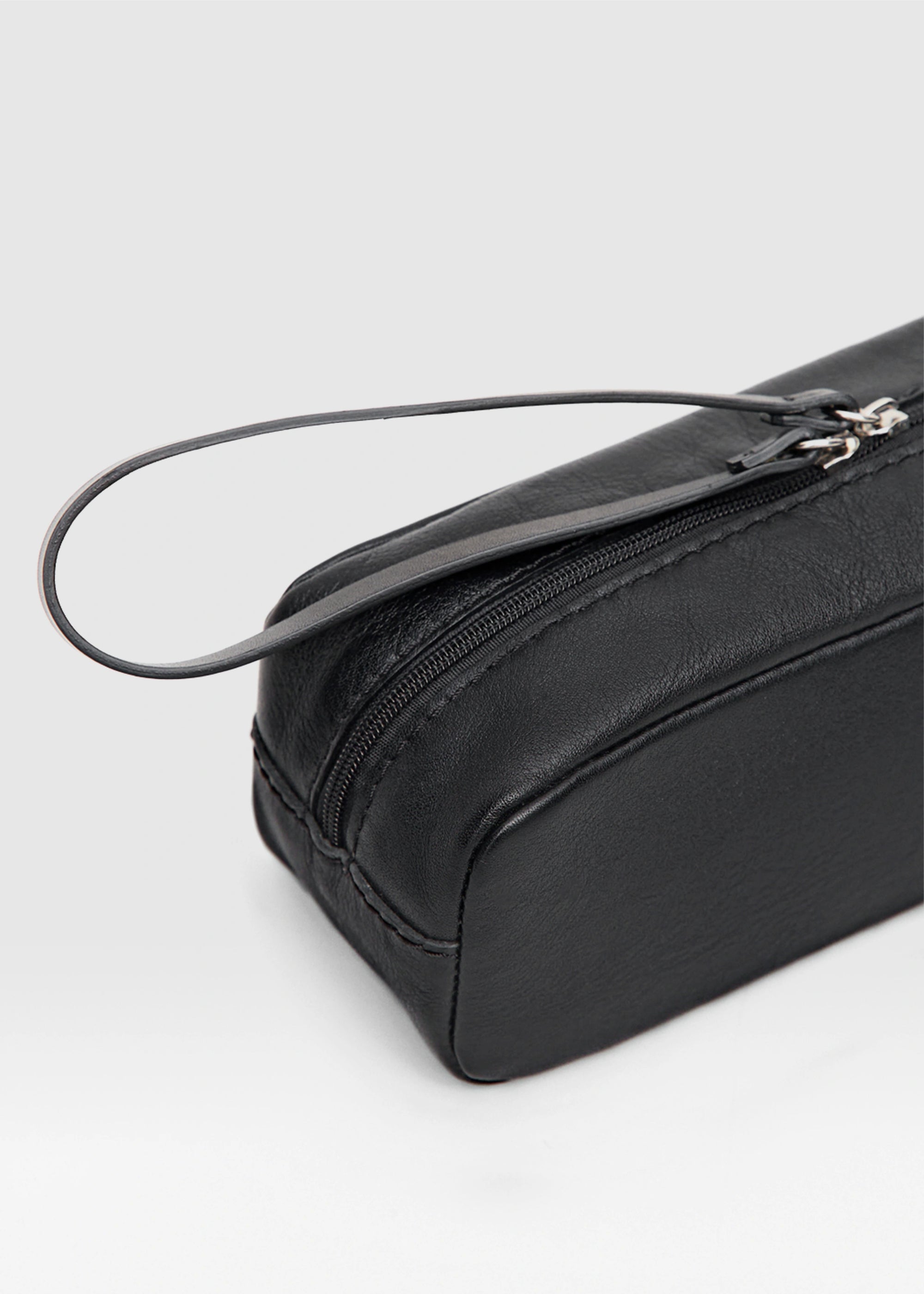 Close-up of the Philini Ellie Cosmetic Bag in black aniline leather, compact rectangular design with zip closure, leather pull, hand-stitched details, and stamped logo. Minimalist and leather makeup bag.