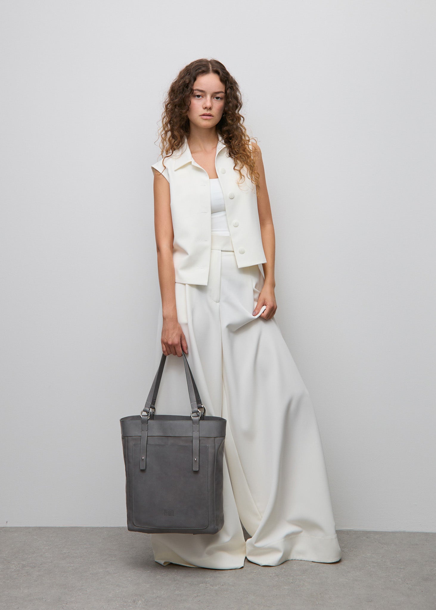 Woman in a white outfit holding a gray tote bag Philini against a plain background