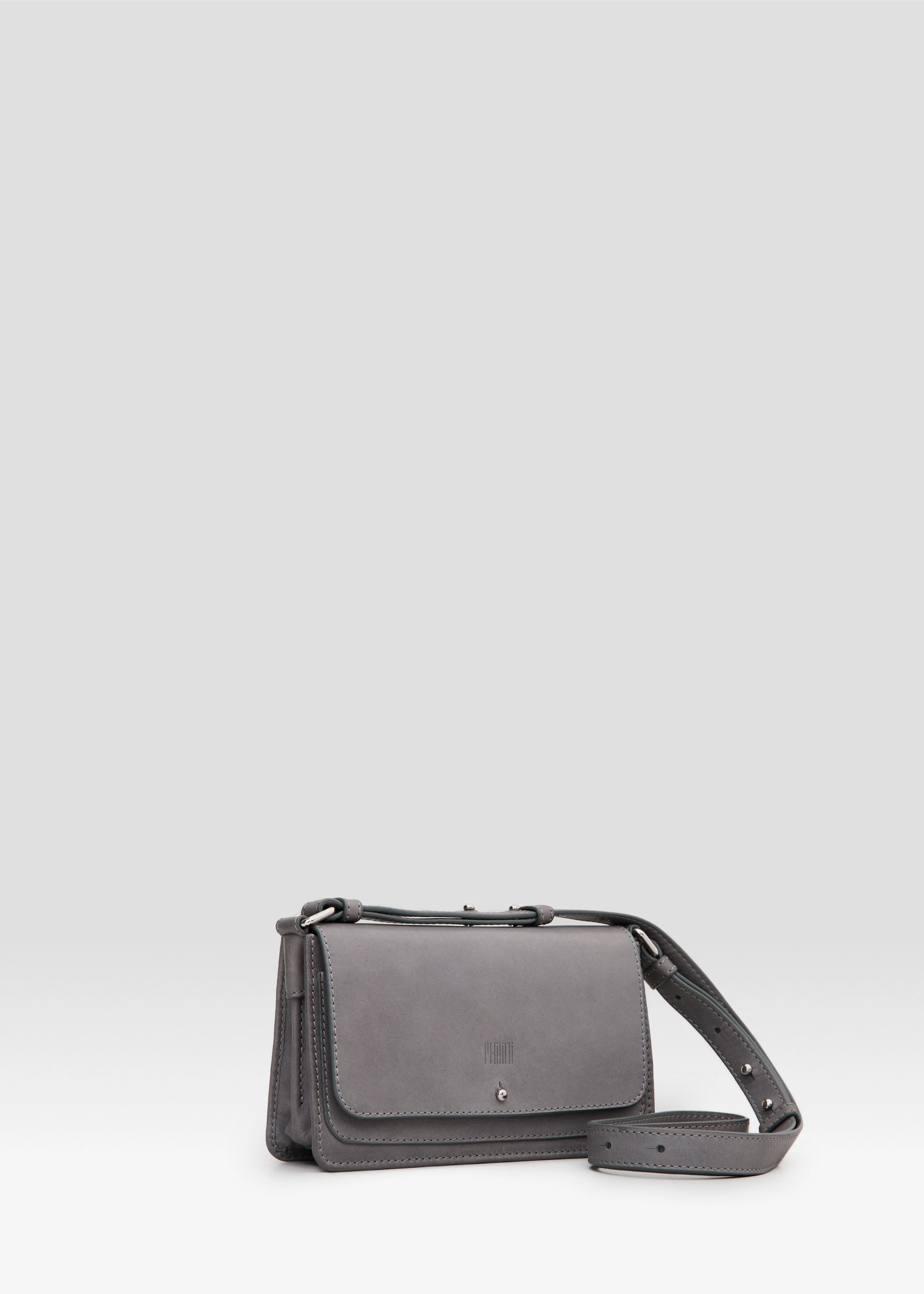 Side view of the Philini Mihaela Wallet Bag in grey Nappa leather, showing softly rectangular shape, front flap with silver cufflink closure, accordion sides, and an adjustable leather strap with silver details. A designer ladies wallet crossbody is functional.
