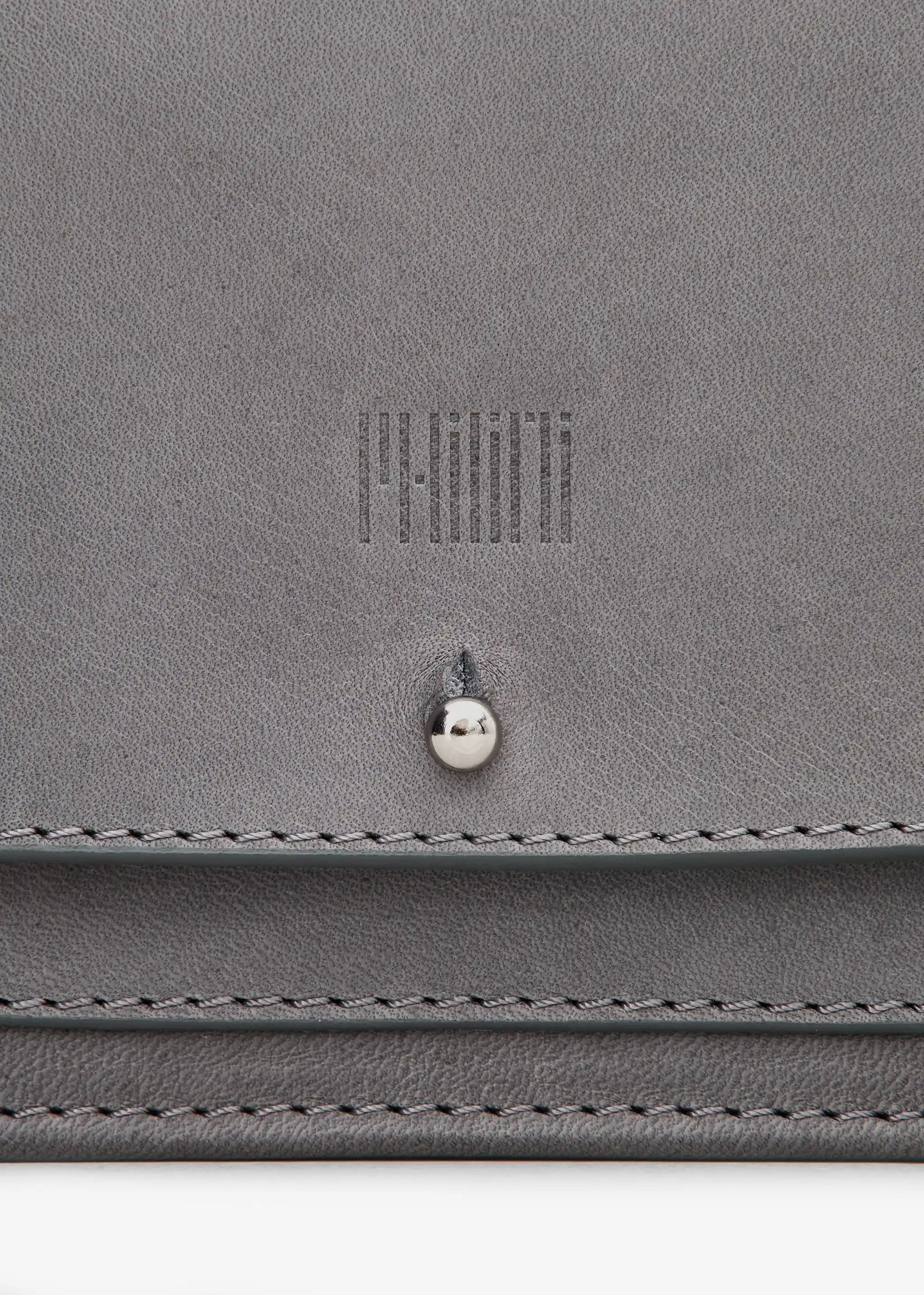 Close-up front view of the Philini Mihaela Wallet Bag in grey nappa leather, featuring a rectangular shape, front flap with silver cufflink closure, stamped logo, and an adjustable strap with silver details. This designer leather wallet crossbody is a luxury accessory.