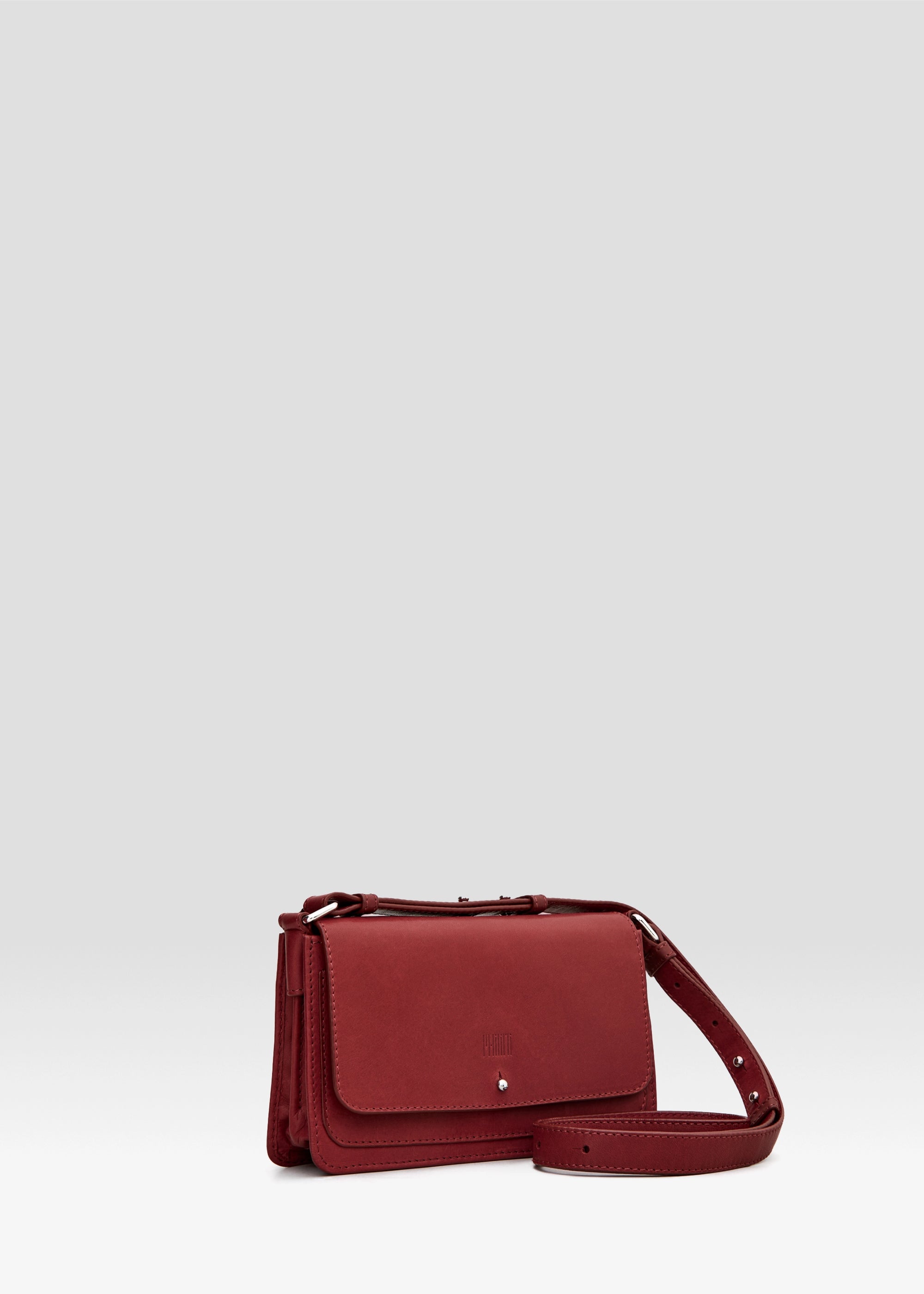 Side view of the Philini Mihaela Wallet Bag in red Nappa leather, featuring a rectangular silhouette, front flap with silver cufflink closure, accordion sides, and an adjustable leather strap with silver details. A wallet crossbody, perfect for luxury and elevated everyday style