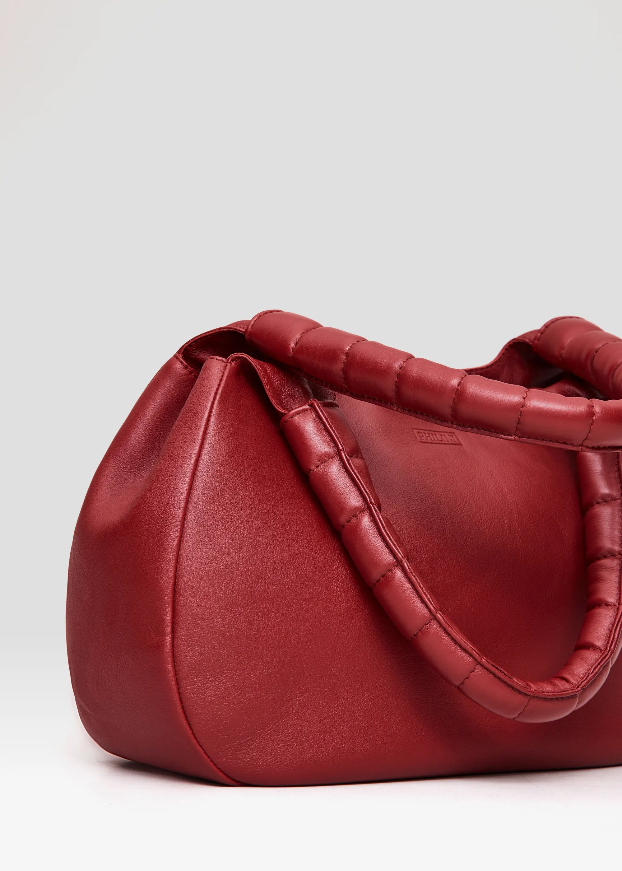Close-up of the Philini Adreann Hobo Bag in red nappa leather, showing two integrated soft handles and a stamped logo. Individually crafted soft leather hobo handbag