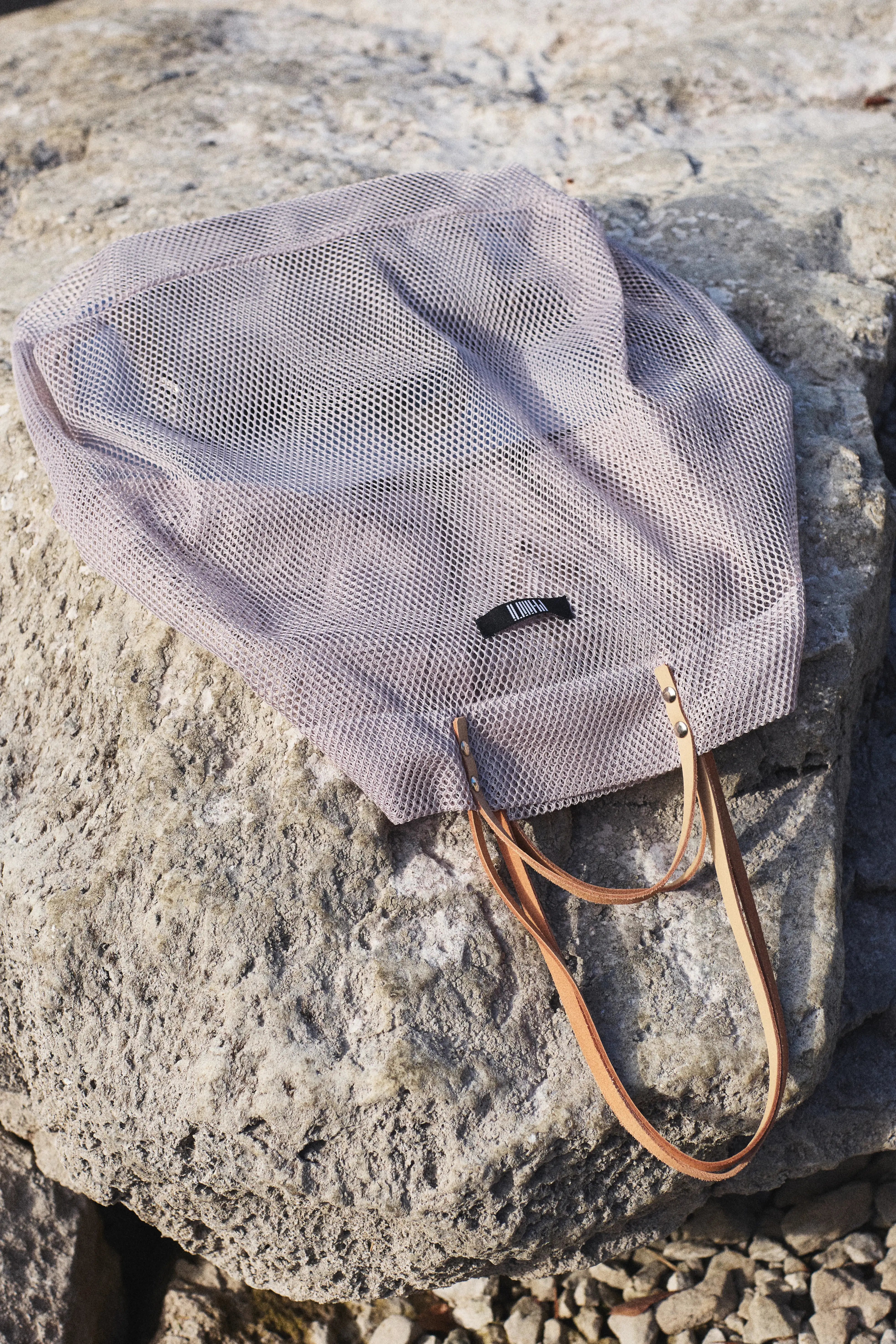 Mesh bag with leather handle on a rocky surface, a new summer shopper from Philini collections. 