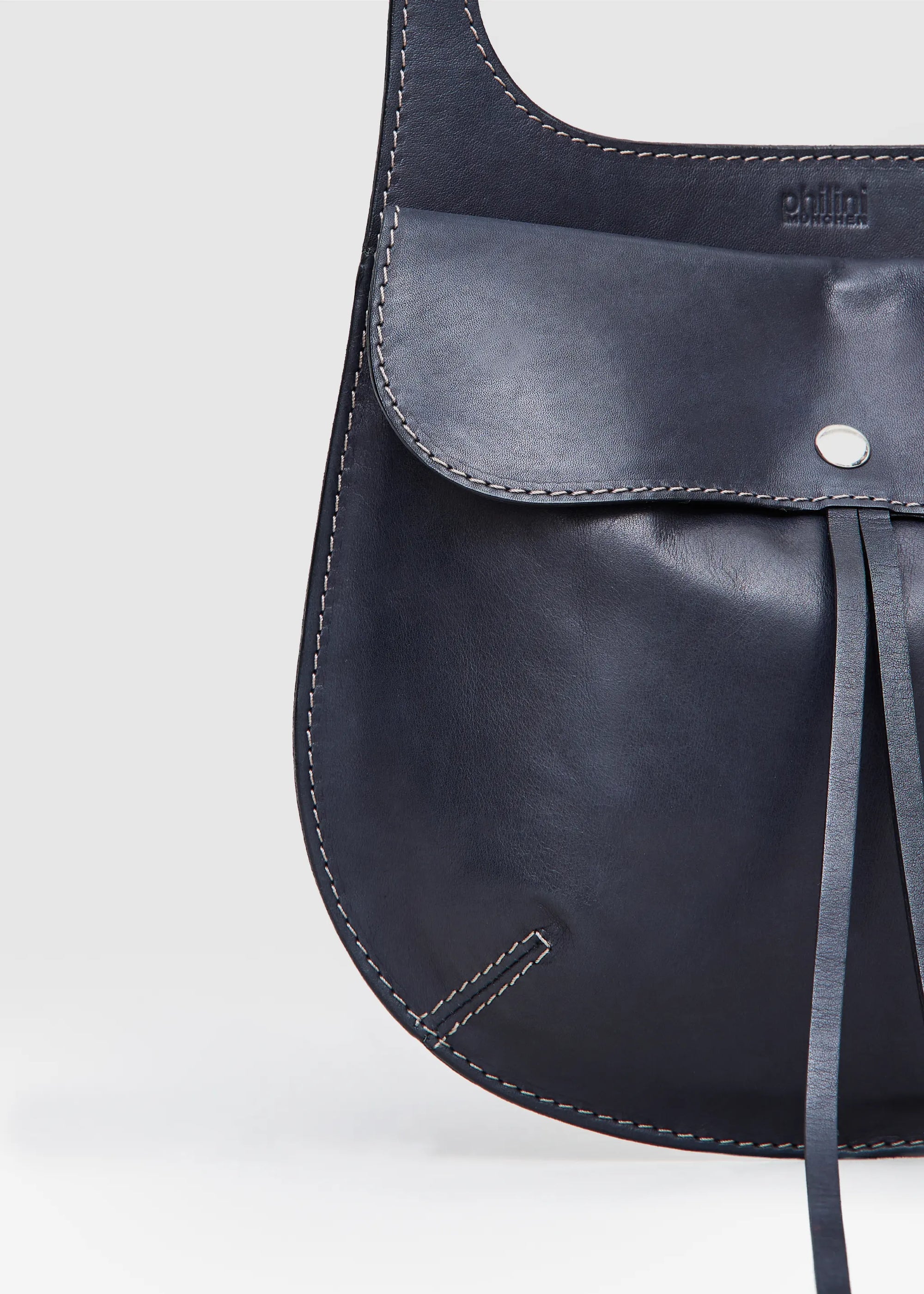 Close-up of the Philini Cowboy Crossbody Bag in black calf leather, rounded saddle silhouette with front flap, snap button closure, and stamped logo. Sustainable minimalistic designer purse