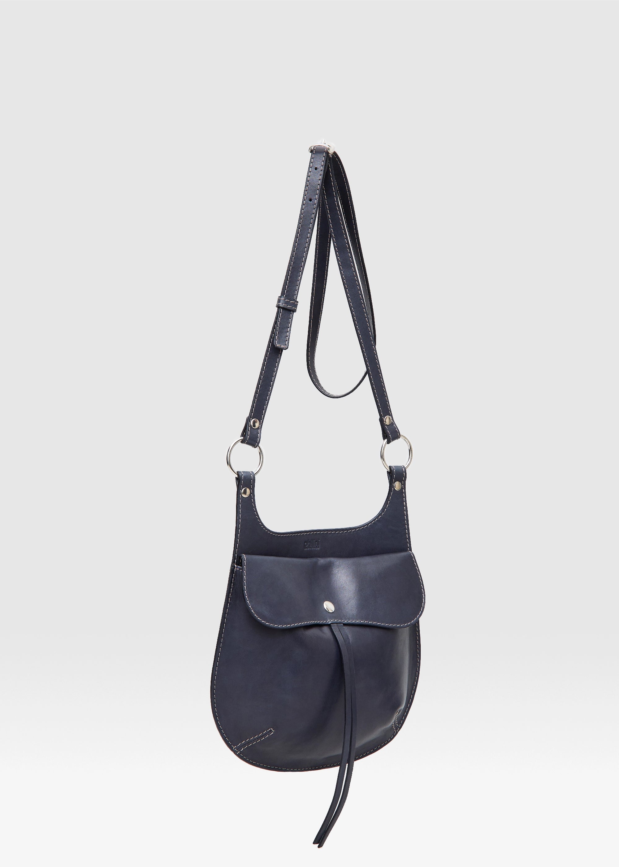 Side view of the Philini Cowboy Crossbody Bag in black calf leather, rounded saddle silhouette with front flap, snap closure, and long adjustable strap. Sustainable mini designer bag for women