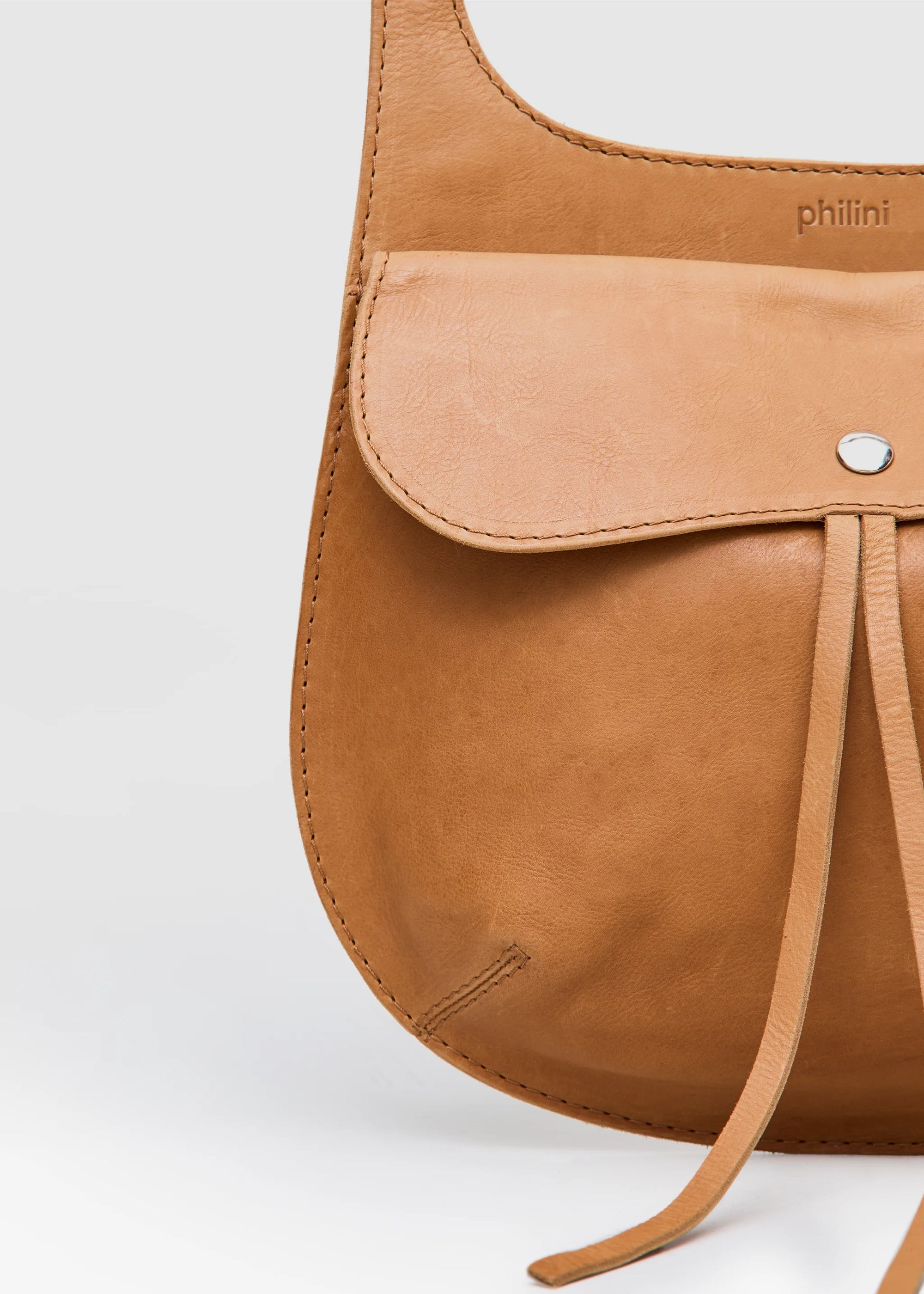 Close-up of the Philini Cowboy Crossbody Bag in cognac calf leather, showing front flap with snap closure, rounded edges, and stamped logo detail. Luxurious minimal leather bag handcrafted in Europe.