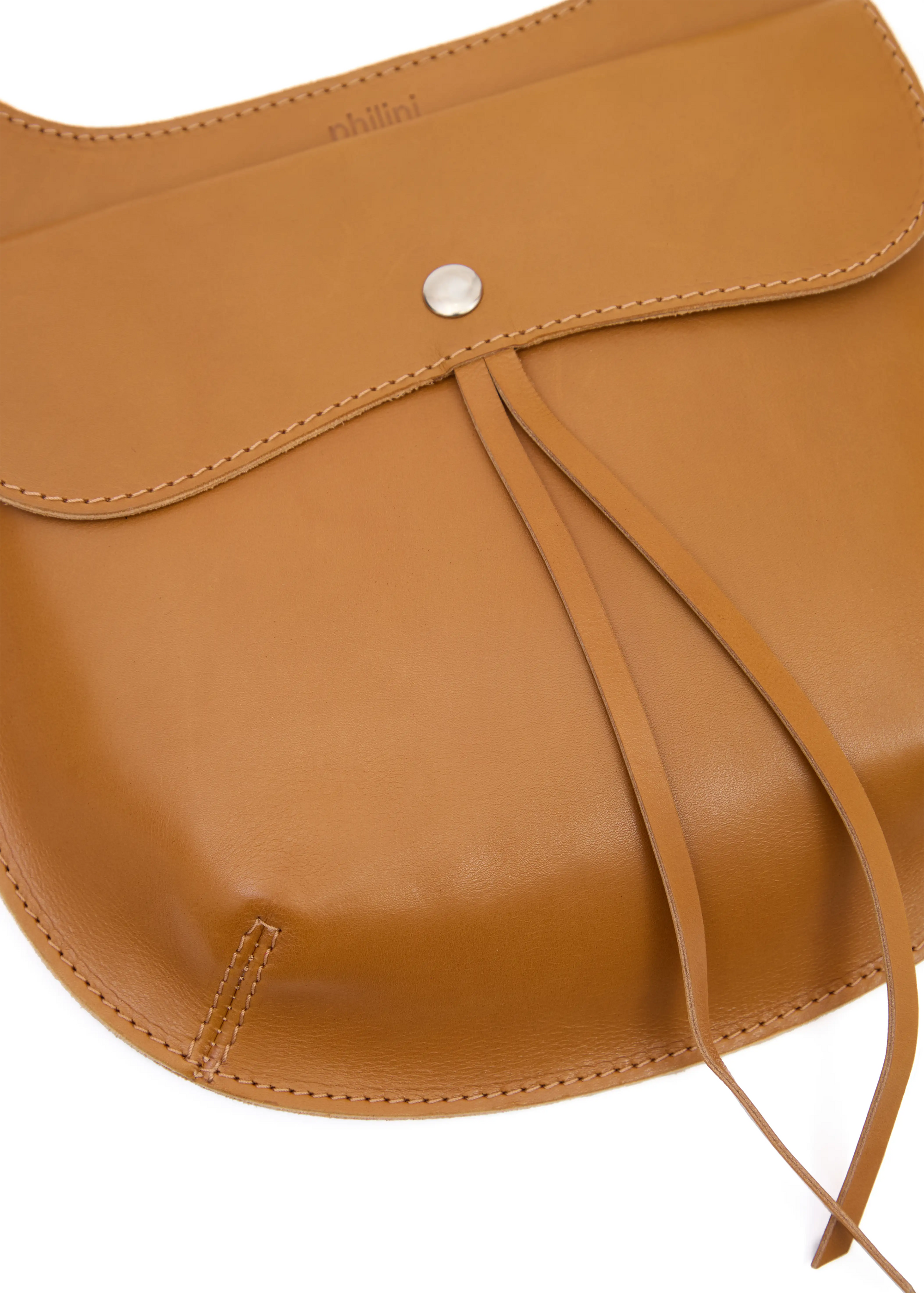 Close-up of the Philini Cowboy Crossbody Bag in cognac calf leather, showing front flap with snap closure, rounded edges, and stamped logo detail. Luxurious minimal leather bag handcrafted in Europe.
