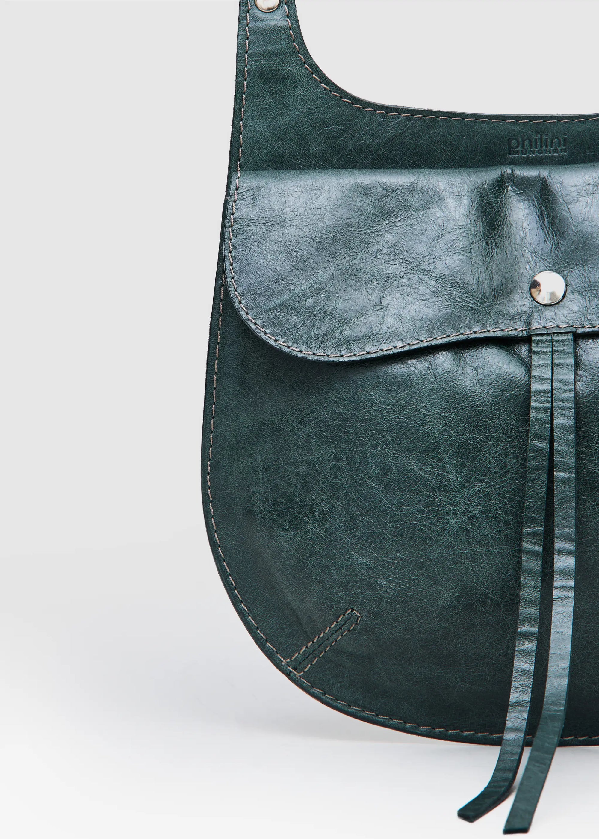 Close-up of the Philini Cowboy Crossbody Bag in dark green calf leather, featuring the front flap with snap button and debossed logo. Sustainable minimal handbag made of premium leather.