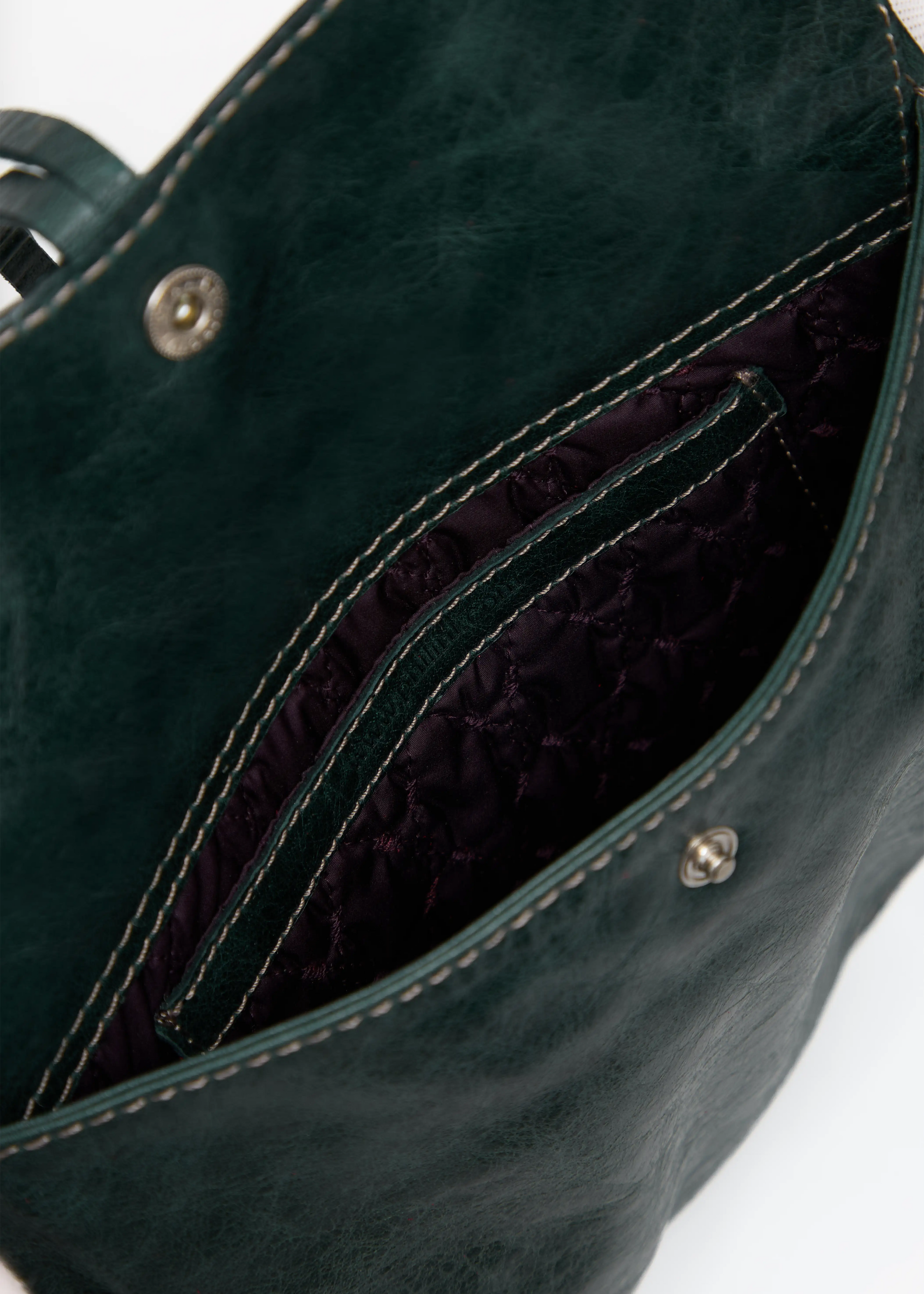 Inside view of the Philini Cowboy Crossbody Bag in dark green calf leather, open flap showing stitched dark lining, small interior pocket, and push-button closure. Functional compact bag