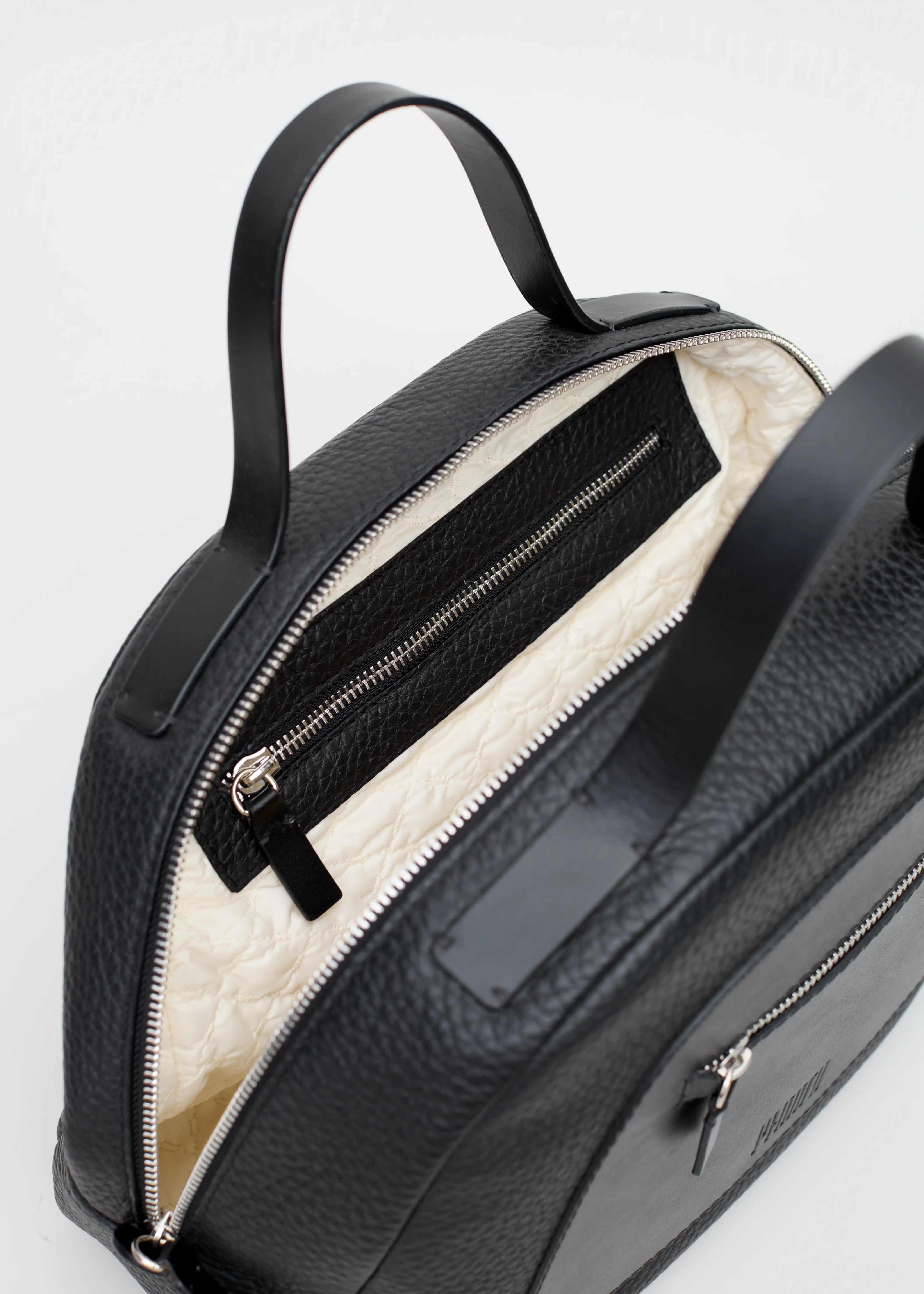 Interior view of the Philini Domi Black Dome Handbag, showcasing hand-stitched full-grain leather short handles, silver rivets and zipper, and a sewn vanilla-patterned lining with spacious zippered compartments.