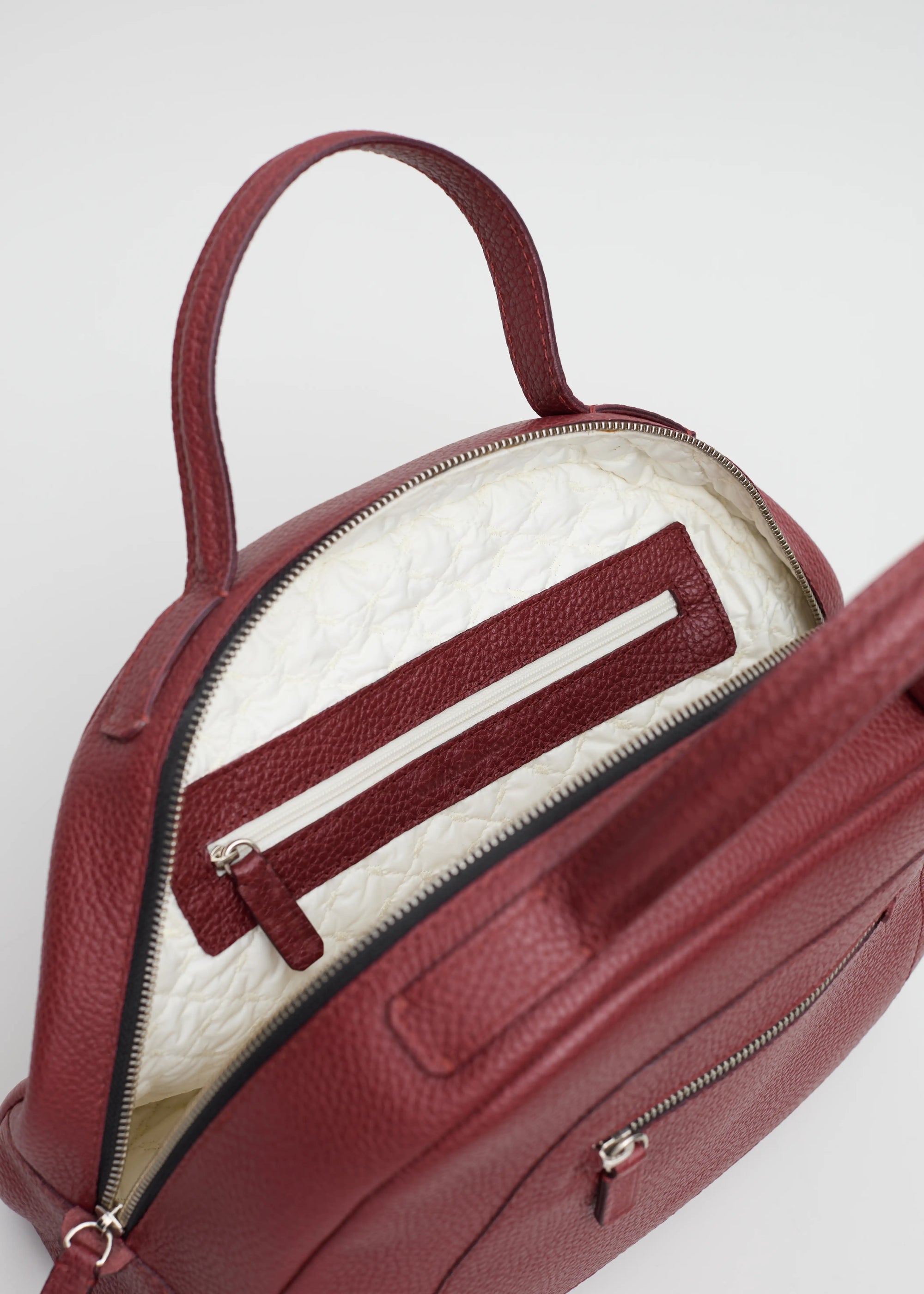 Interior view of the Philini Domi red Handbag in dome shape, handcrafted from calf leather and finished with short leather handles, silver rivets, and a zipper closure. The interior features a vanilla-colored lining and zippered inner pockets.