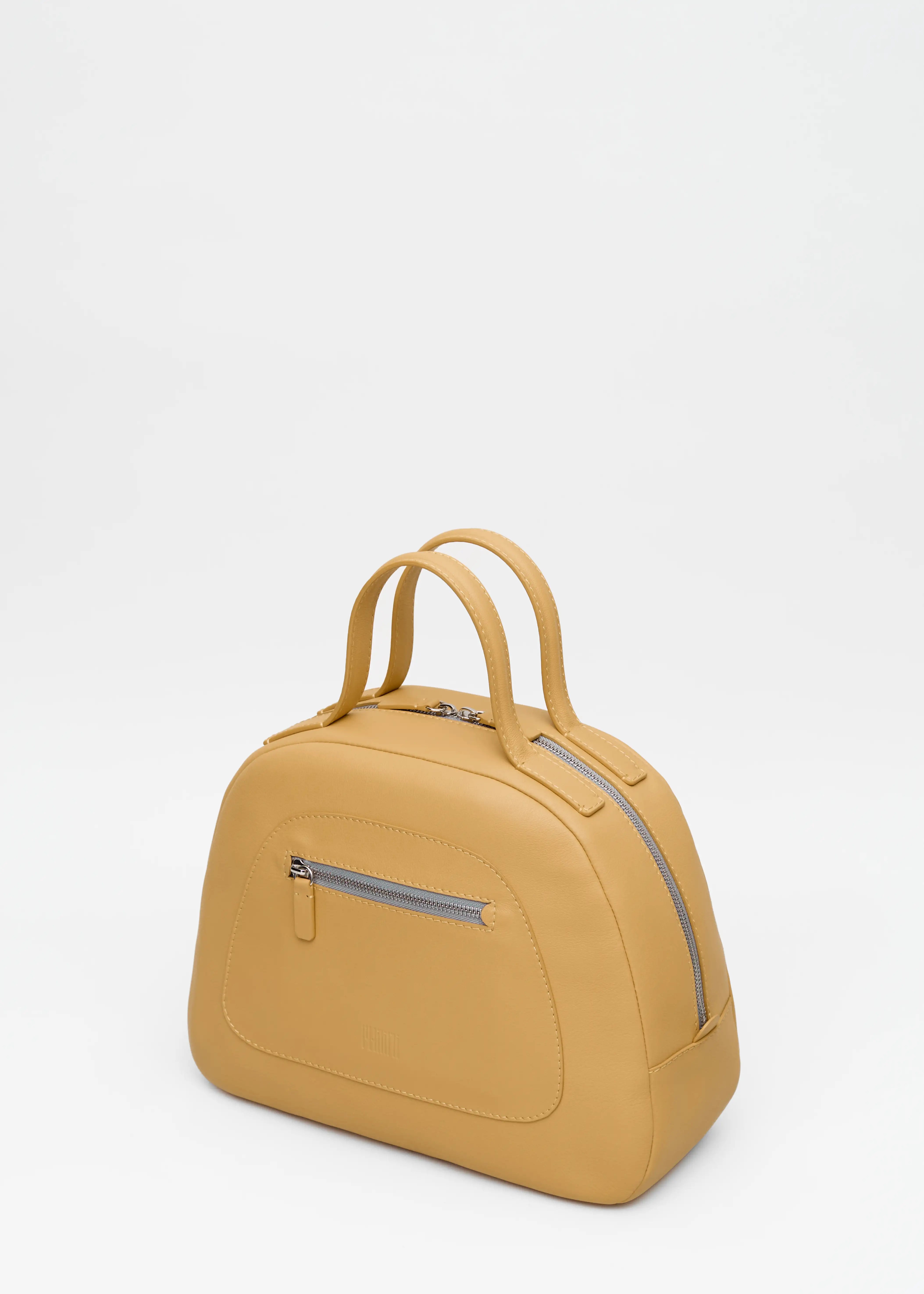 Side view of the Philini Domi Handbag in yellow nappa leather, showcasing the dome shape, short handles, silver rivets, front zip pocket, and zipper closure. This handcrafted luxury leather handbag is a sustainable craftsmanship for everyday elegance