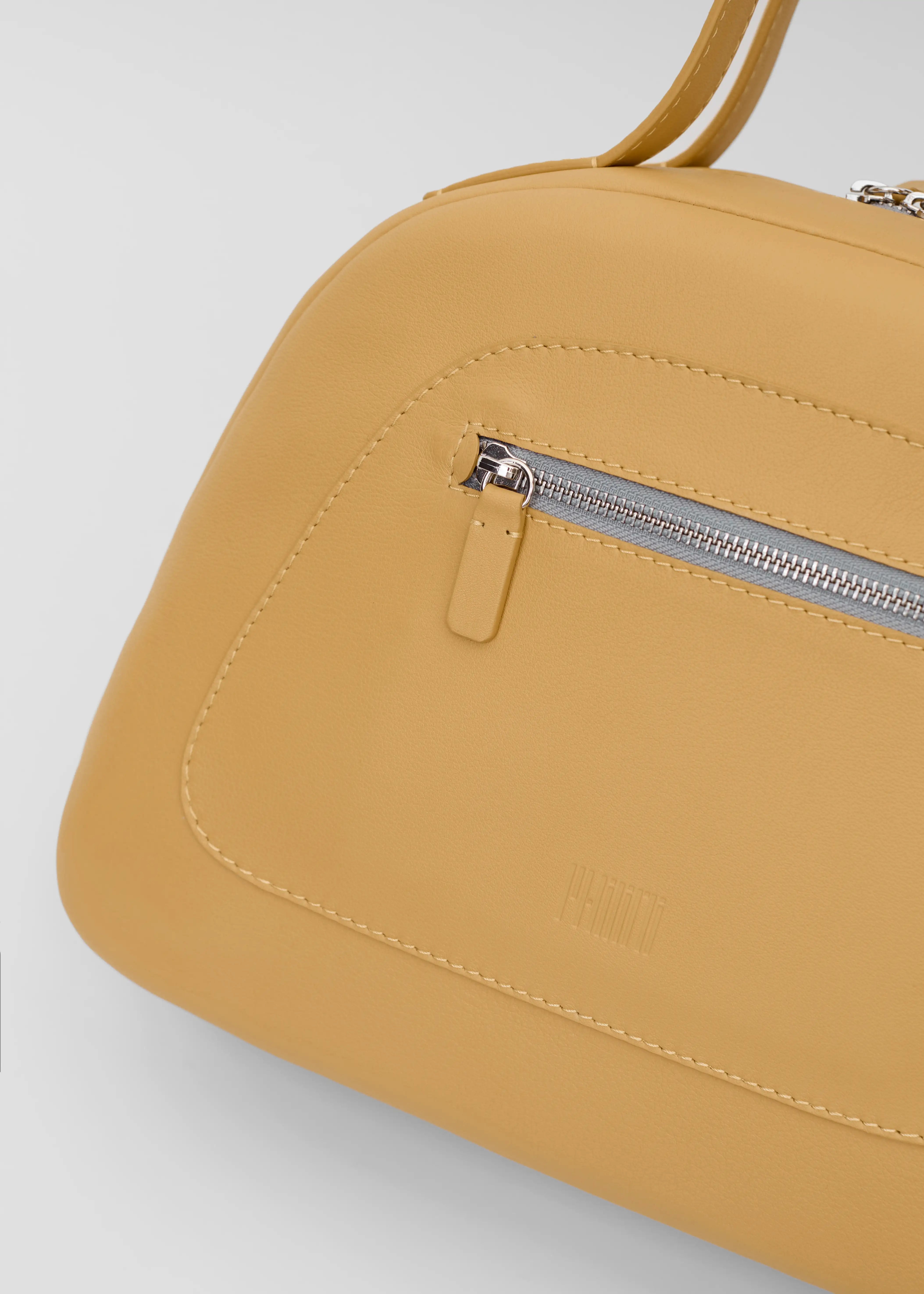 Detailed view of the yellow Philini Domi Handbag in soft nappa leather, showing dome shape, short handles, front zip pocket, and silver hardware. A stylish and handcrafted everyday leather bag 