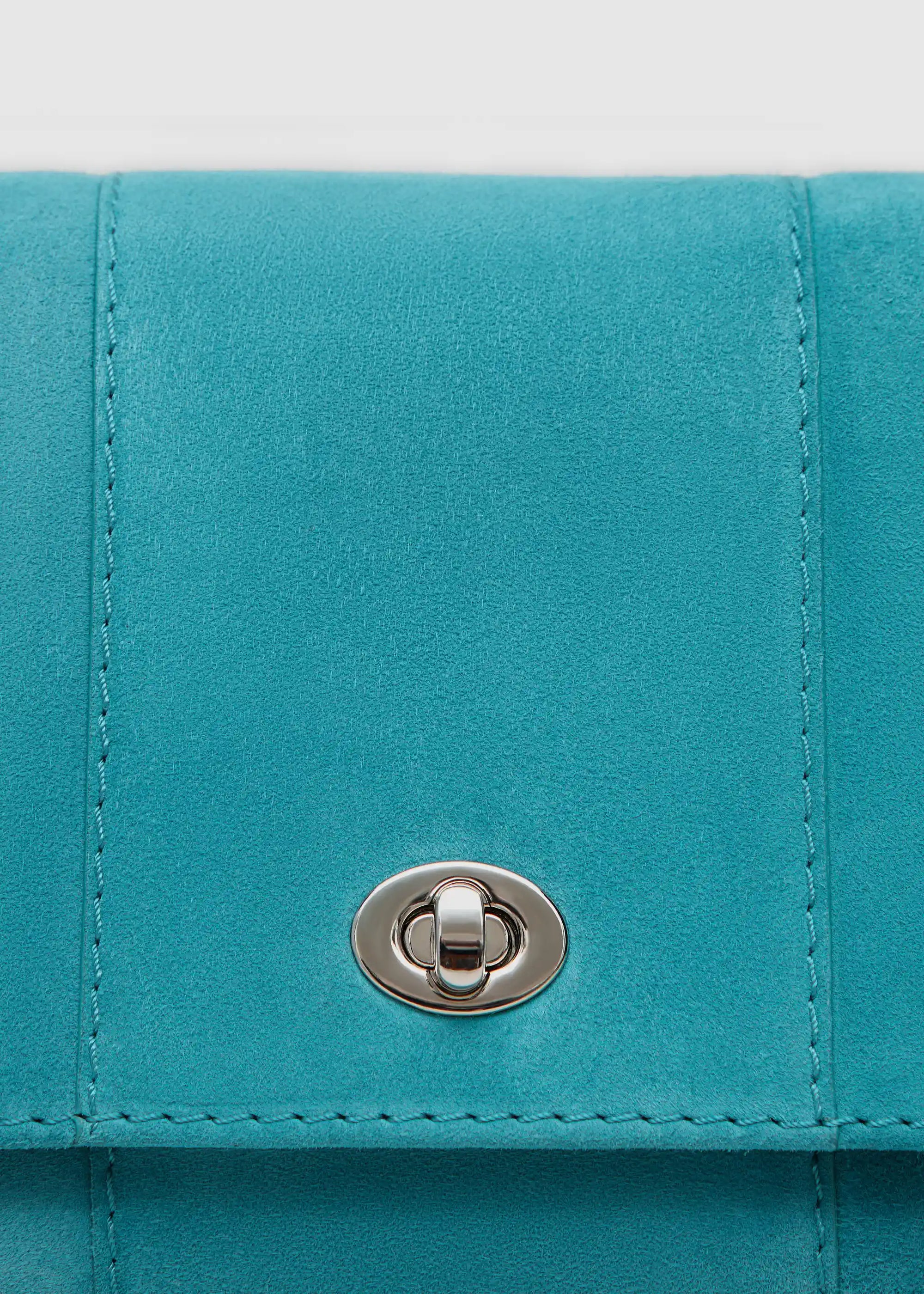 Close front view of the Philini Marina Mini Crossbody Bag in turquoise suede leather, showing front flap with silver clasp and carabiner-attached chain handle. Elegant and luxurious soft-touch accessory
