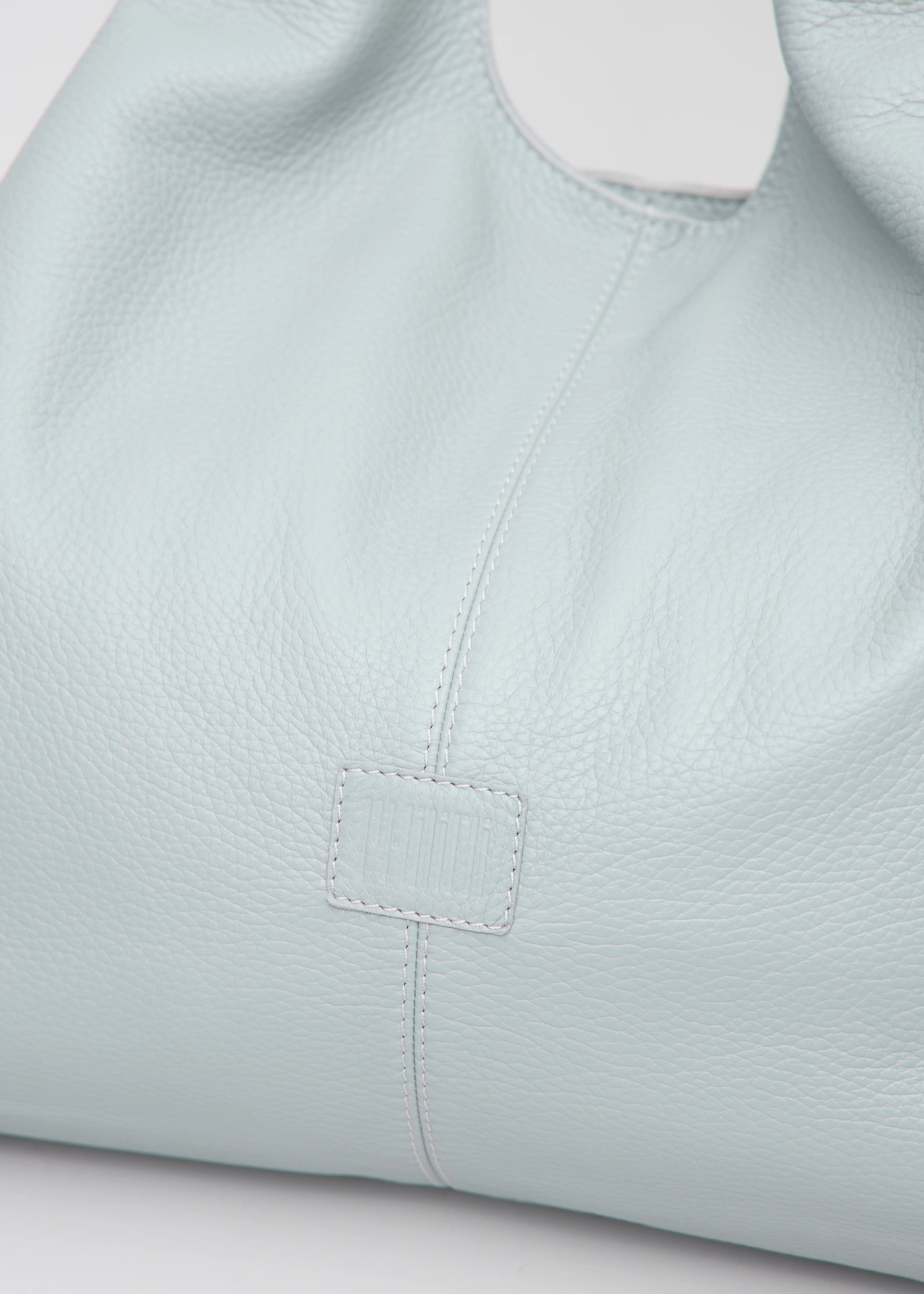 Close-up of the Philini Melanie Hobo Bag in grey buffalo leather, highlighting the leather patch with stamped logo, and premium leather texture. Soft full-grain leather hobo tote, luxury minimalist shoulder bag