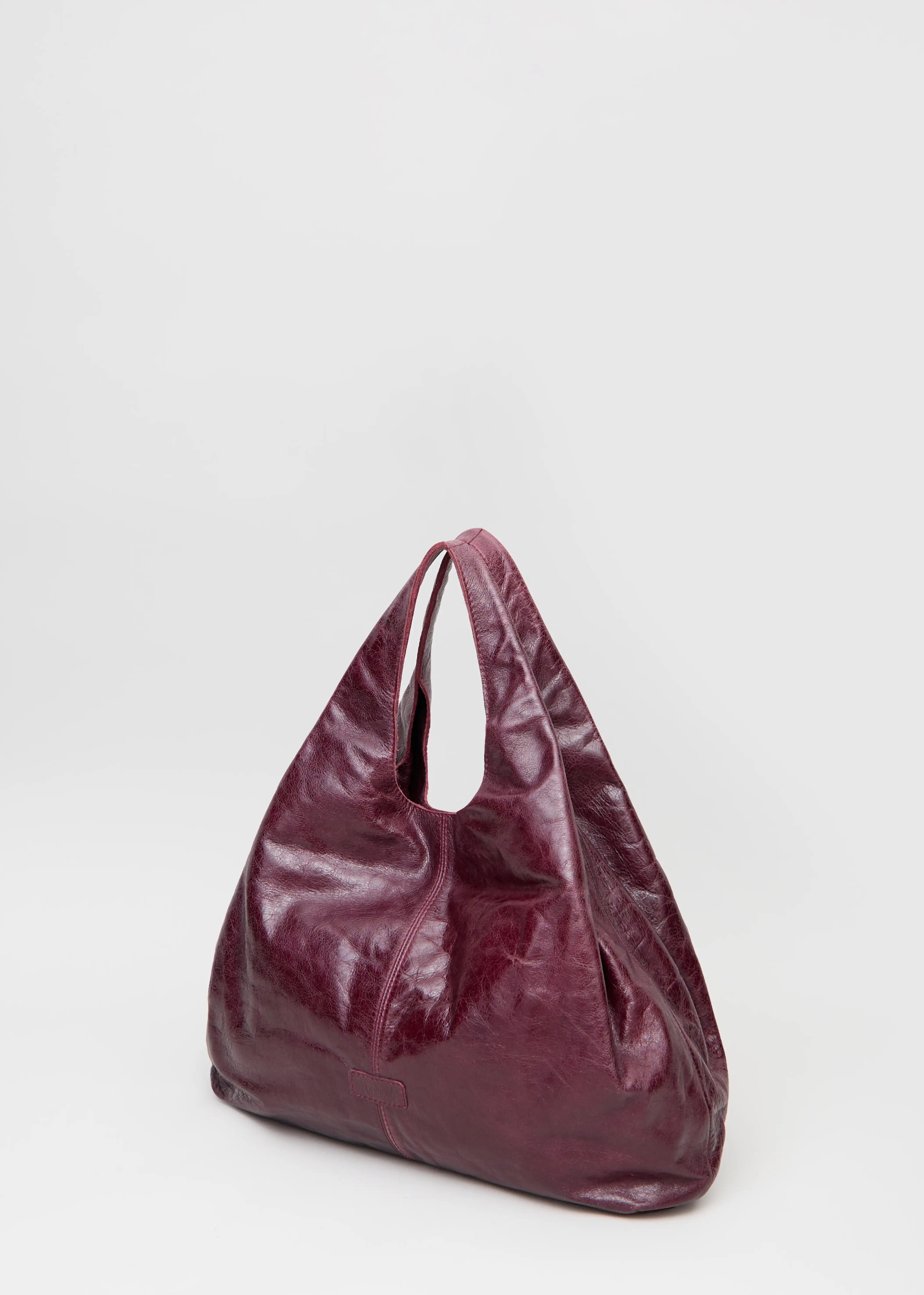 Side view of the Philini Melanie Hobo Bag in burgundy calf leather, featuring two top handles and a leather patch with stamped logo. High-quality slouchy hobo bag