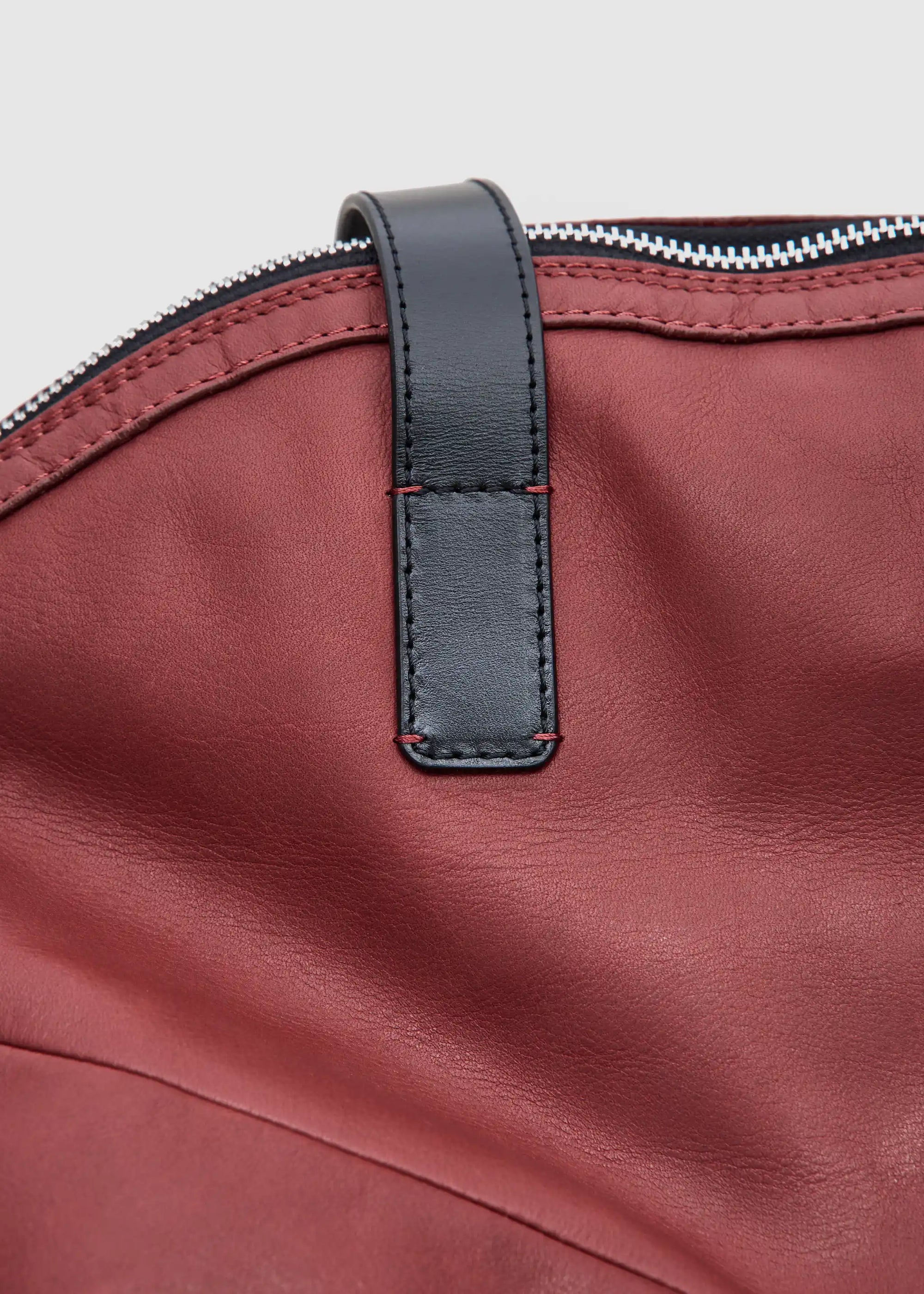 Close-up of the Philini Nataly Handbag in bordeaux aniline calf leather, round silhouette with stamped logo and premium leather texture. Luxury red leather shoulder bag a designer accessory