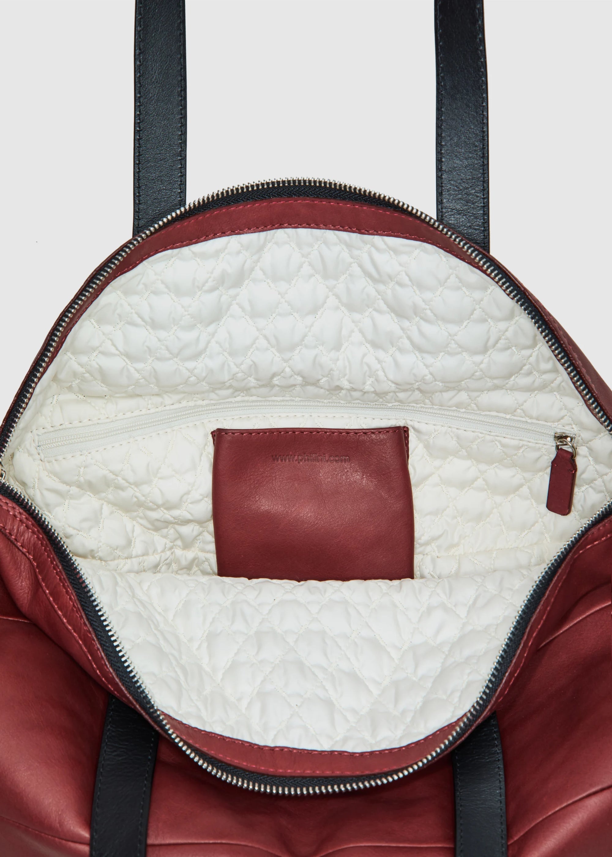 Inside of the Philini Nataly Handbag in bordeaux aniline calf leather, round silhouette with stamped logo and premium leather texture. Luxury red leather shoulder bag a designer accessory