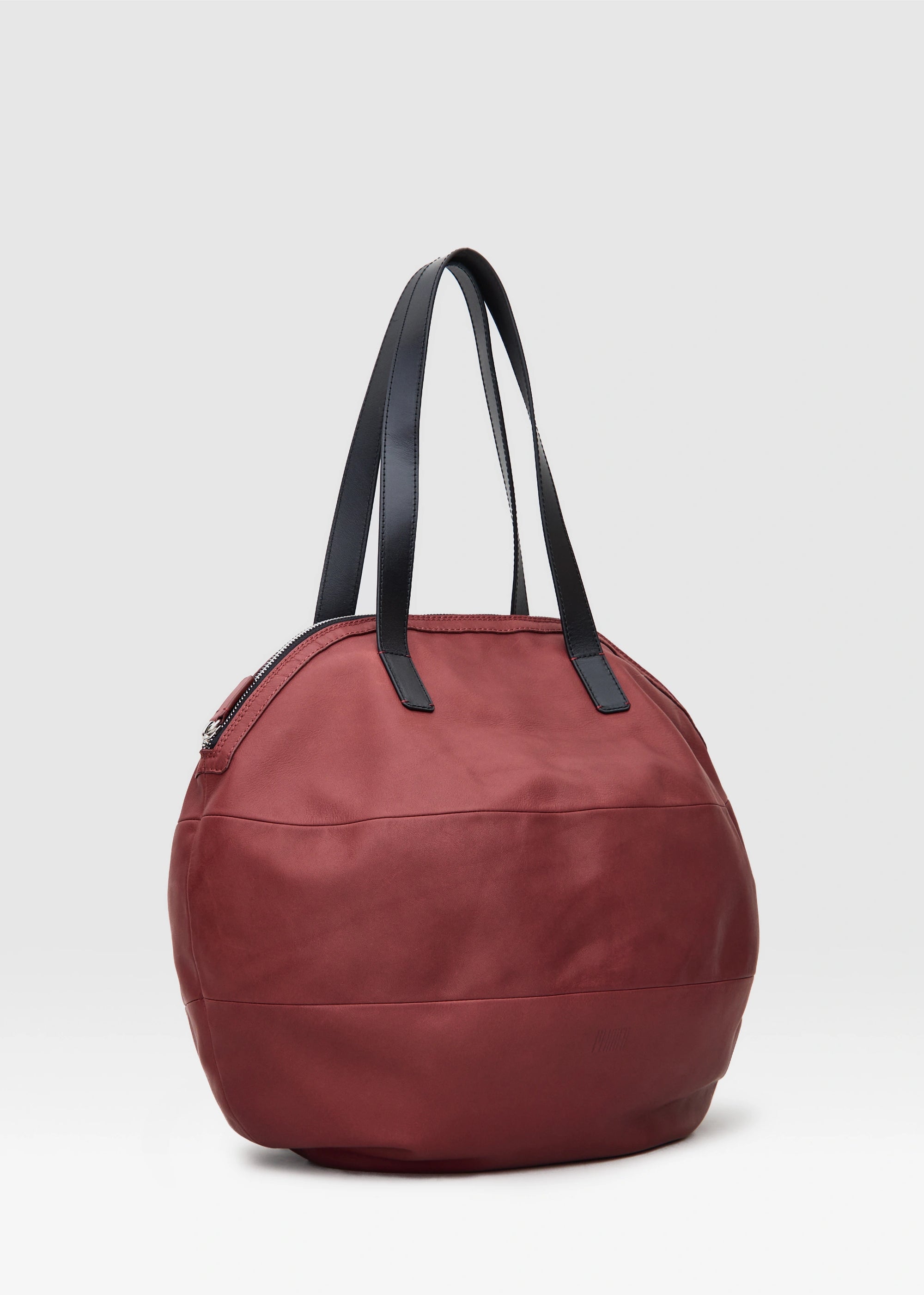 Side view of the Philini Nataly Handbag in bordeaux aniline calf leather, round silhouette with two black handles and bronze zipper. Unique red designer handbag