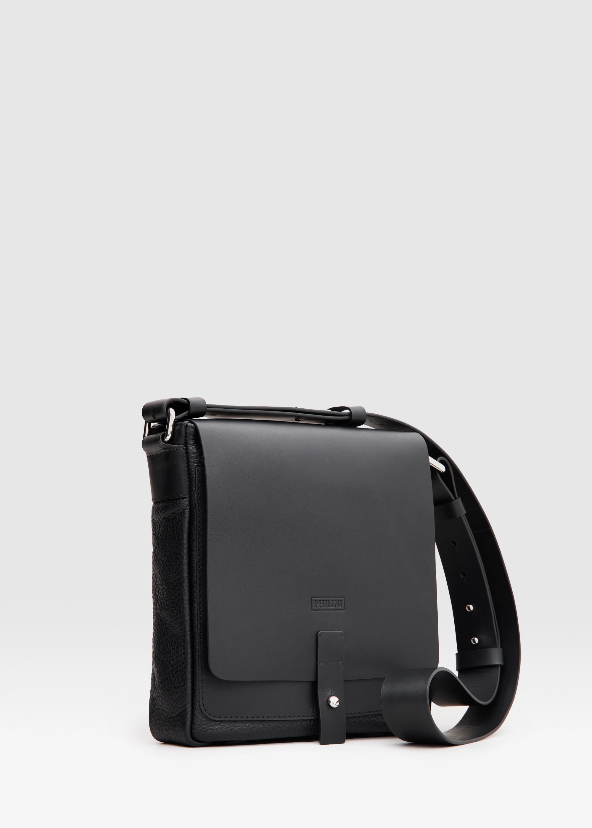 Angled view of the Olga black messenger bag, handcrafted from full-grain and buffalo leather with a square shape, front flap, and silver cufflink closure. A sustainable, luxury accessory for women.