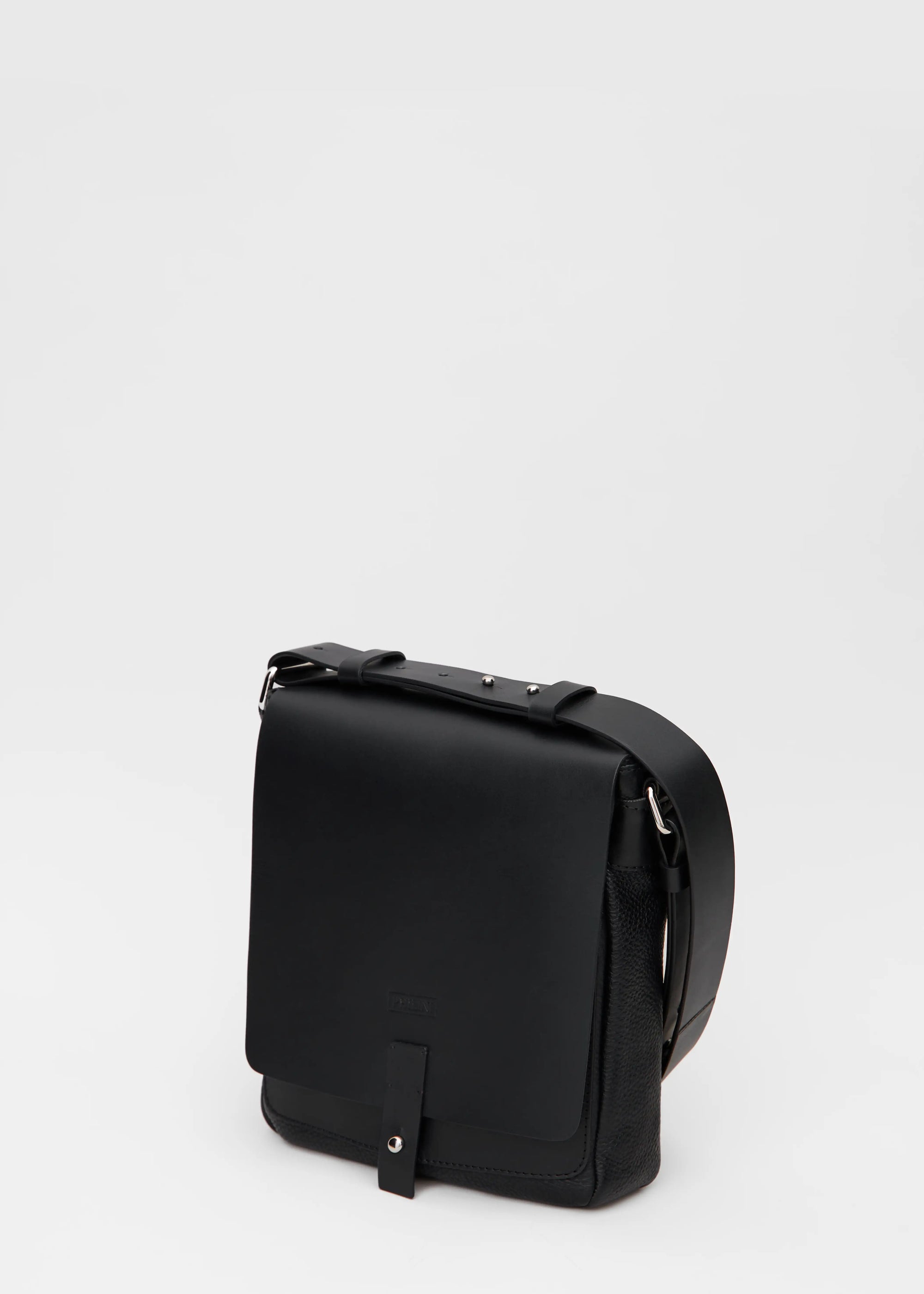 Angled view of the Olga black messenger bag, handcrafted from full-grain and buffalo leather with a square shape, front flap, and silver cufflink closure. A sustainable, luxury accessory for women.