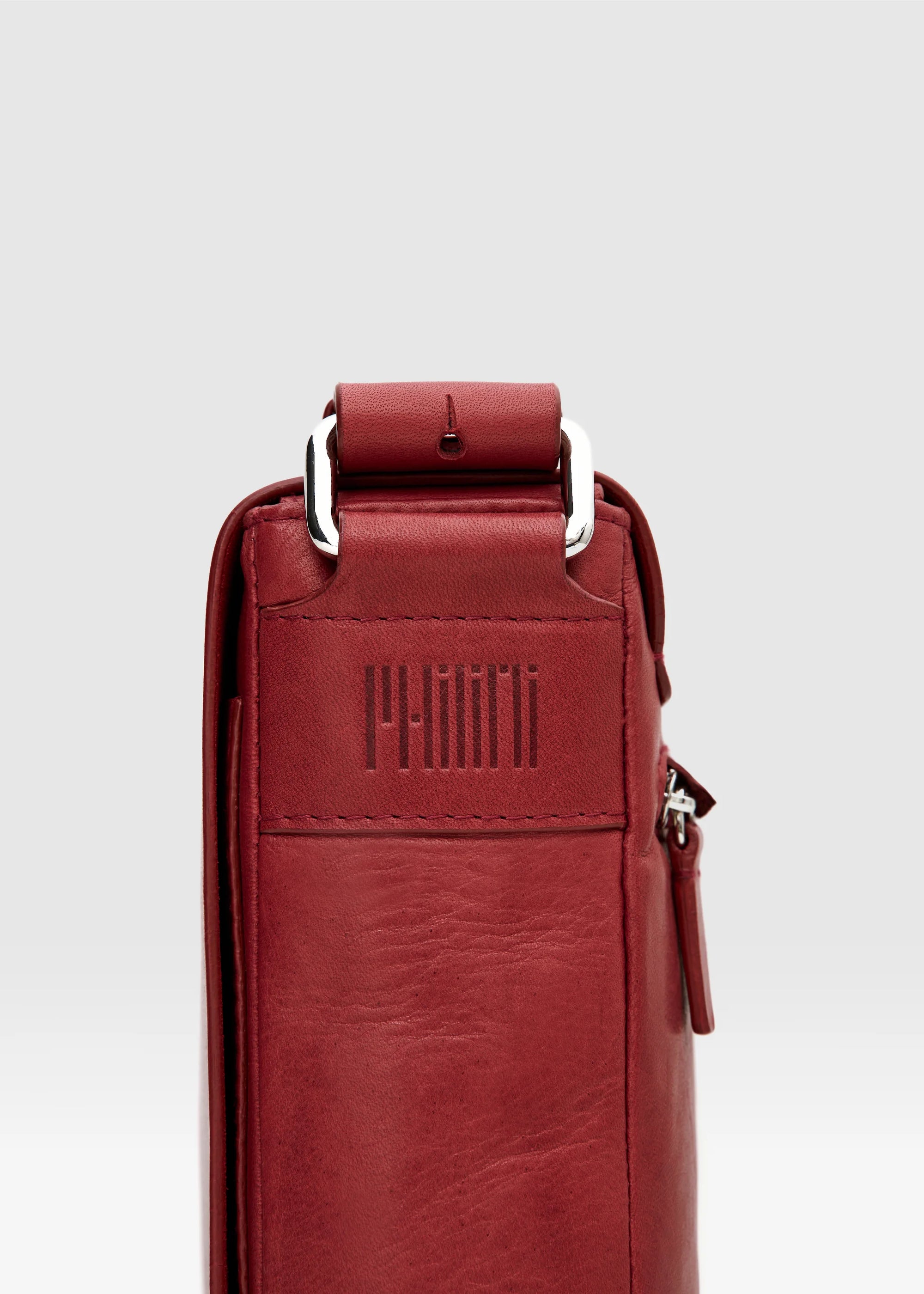Close-up of the Philini Olga shoulder bag in red aniline nappa leather, showing the stamped logo, silver hardware attaching the leather strap.