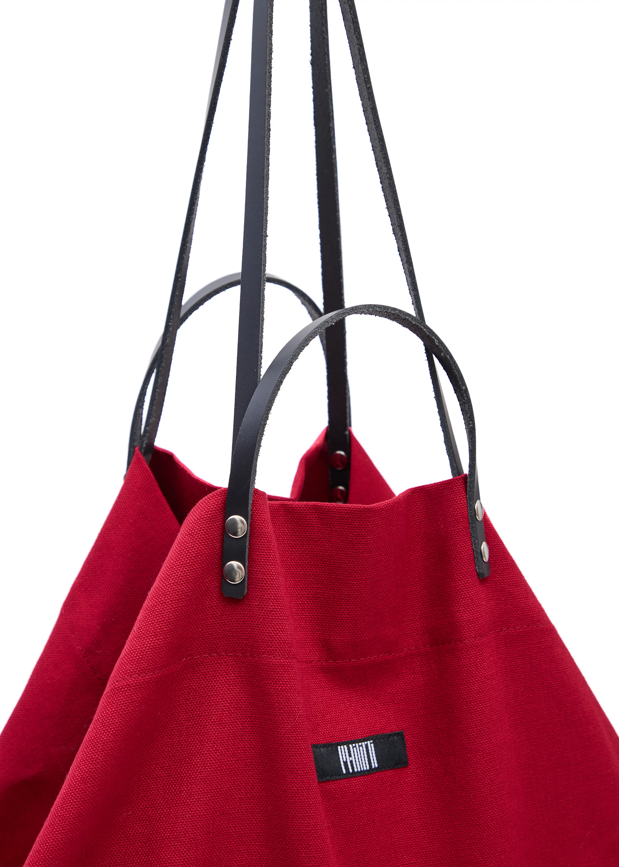 Close-up of the Philini Red Shopper bag, highlighting two pairs of calf leather handles with silver hardware, and top button closure on a bold red cotton fabric