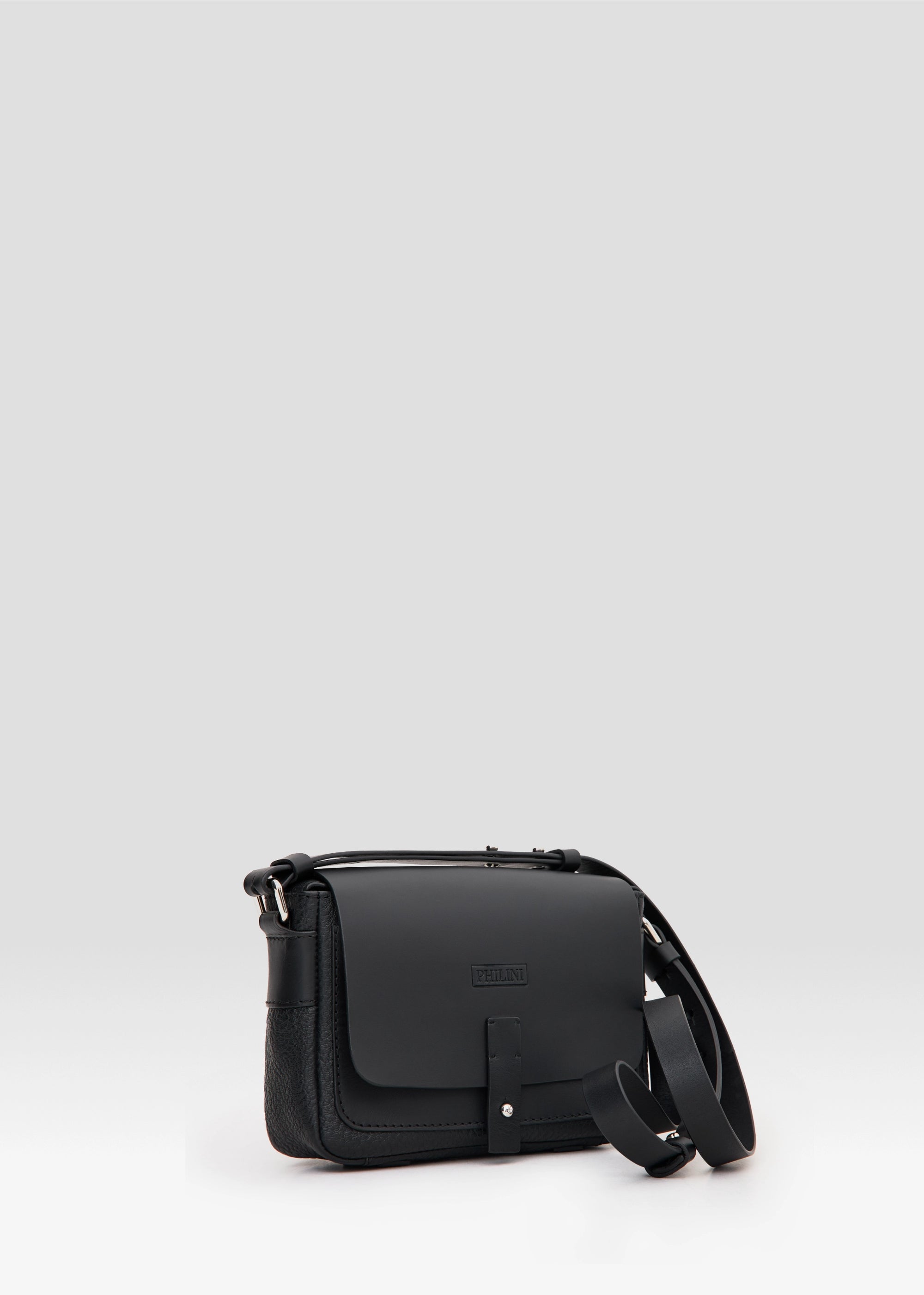 Side view of the Philini Whitney Black Leather Bag, a handcrafted designer bag with a rectangular shape, premium full-grain leather front flap, silver push-button closure, and an adjustable strap with silver accents. Designed in Germany from sustainable materials.