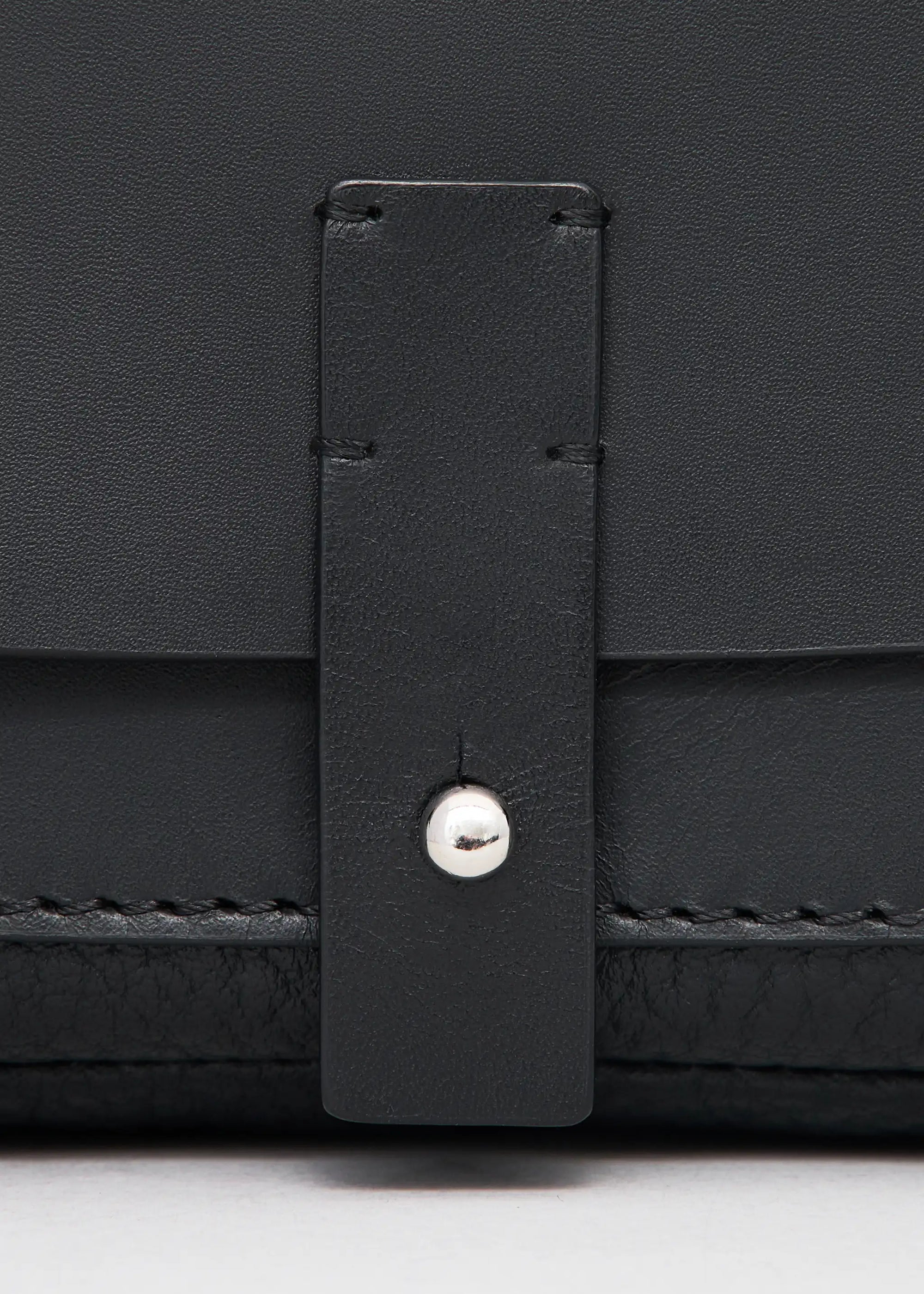 Close-up front view of the Philini Whitney Black Leather Bag, a rectangular handcrafted designer bag with a premium leather flap, silver push-button closure, adjustable strap, and protective leather pads. A sustainable and elegant accessory