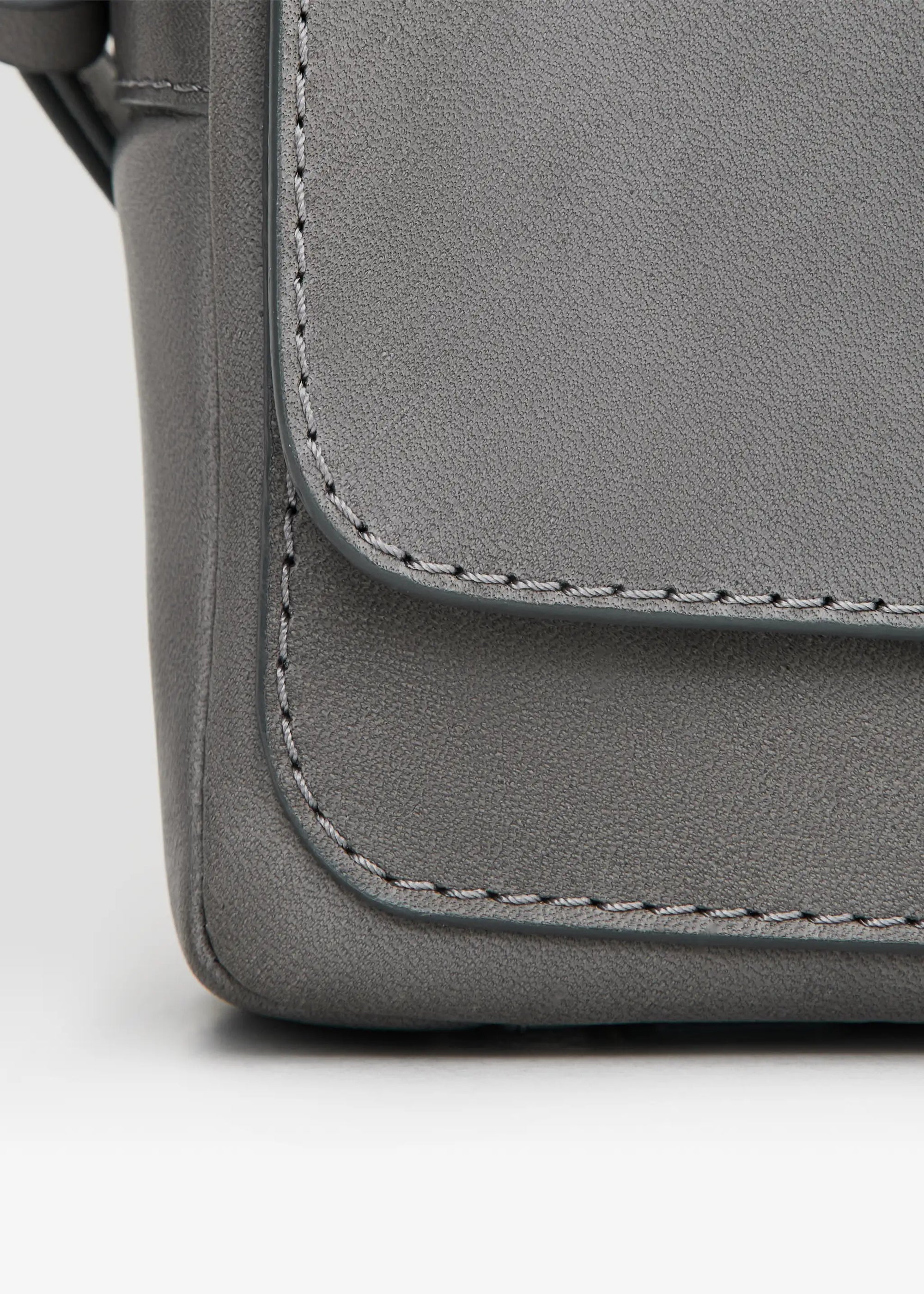 Close side view of the grey Philini Whitney Mini Crossbody Bag in nappa leather, featuring a vertical rectangle shape, silver cufflink flap, adjustable strap, and hand-stitched details. A compact, handcrafted luxury leather crossbody for sustainable style and everyday elegance.