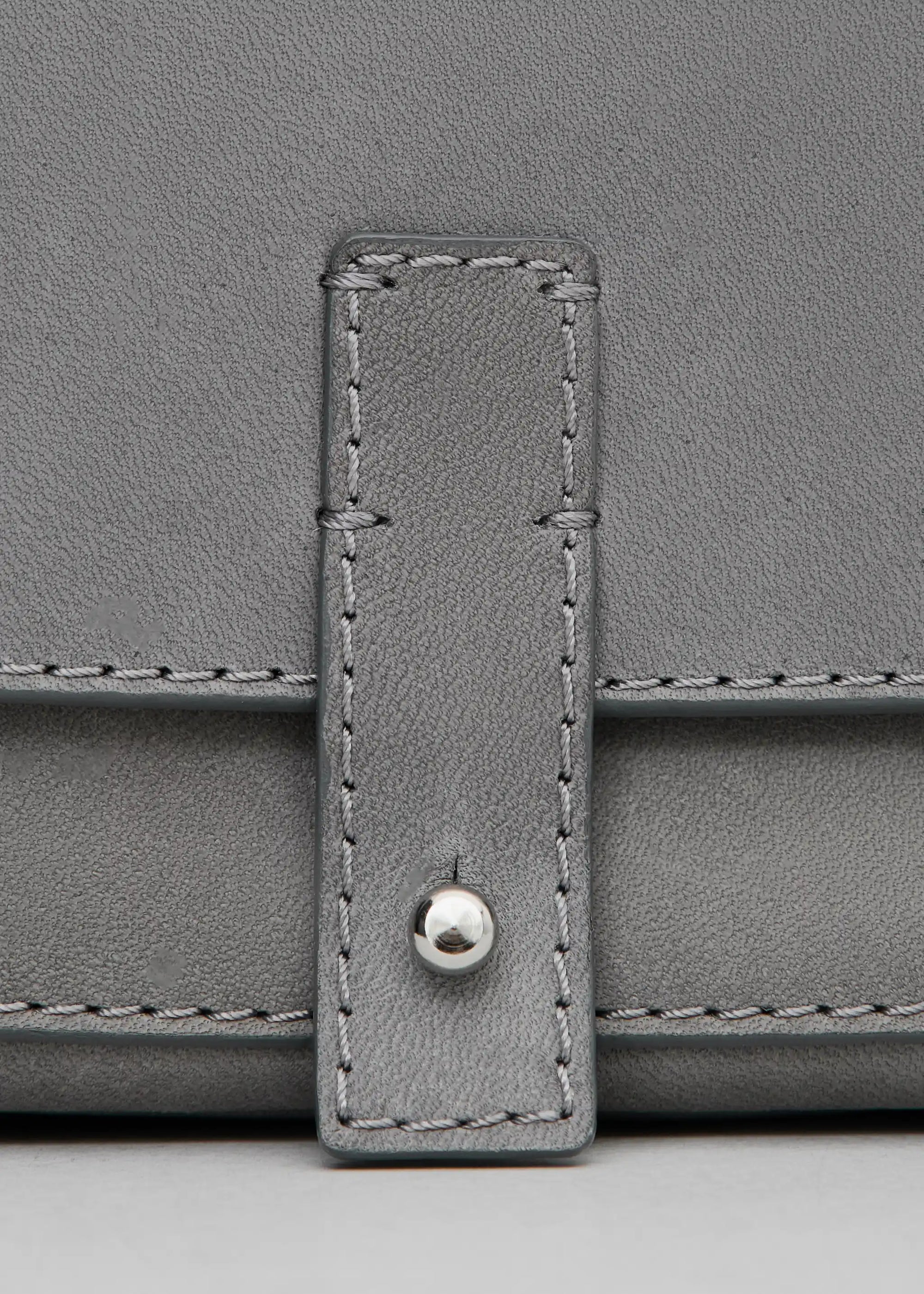 Close front view of the grey Philini Whitney Mini Crossbody Bag in nappa leather, showing hand-stitched details, silver cufflink closure, and adjustable strap. A compact handmade leather bag.