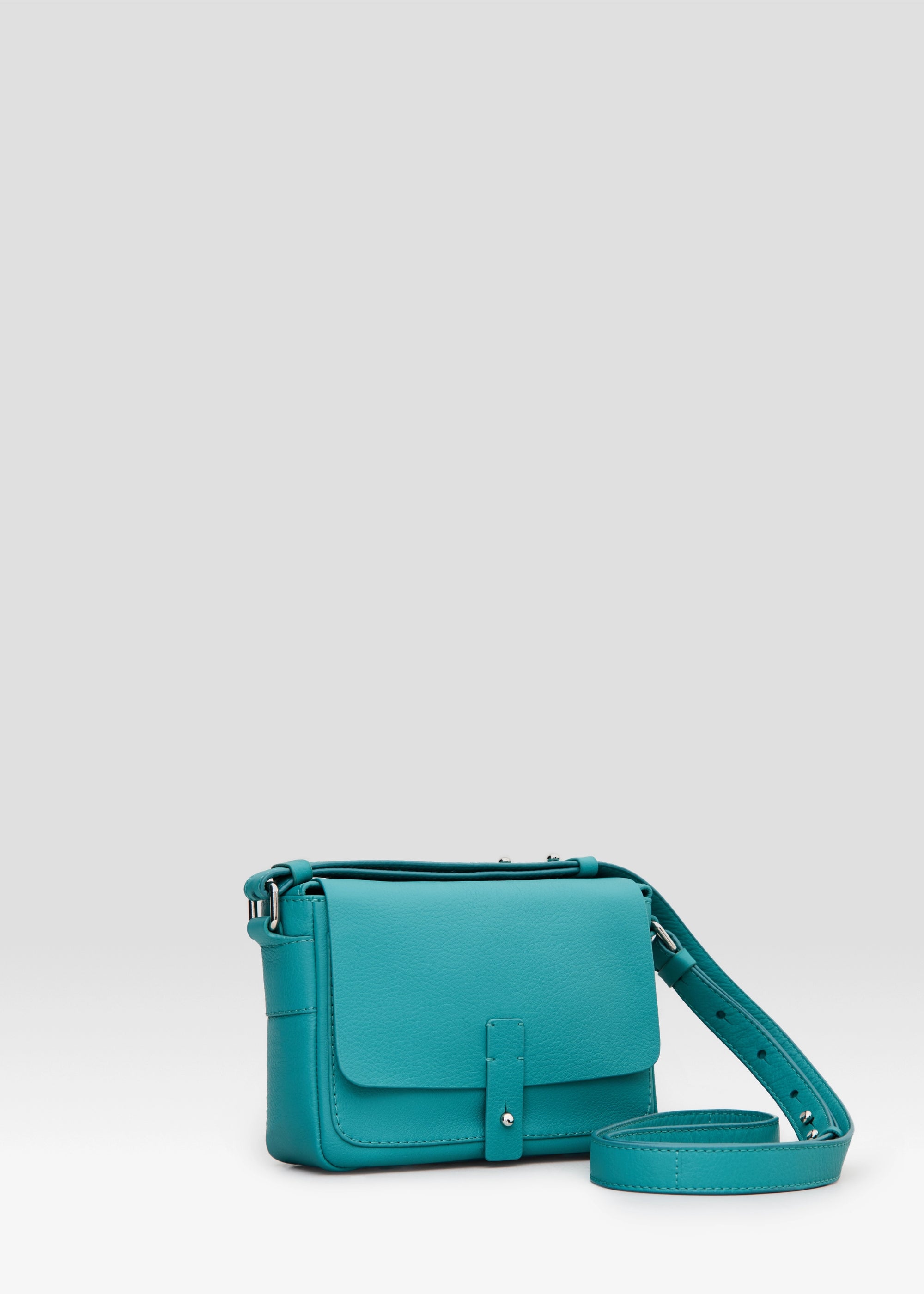 Side view of the Philini Whitney Mini Crossbody Bag in turquoise nappa leather, featuring a vertical rectangular shape, silver cufflink flap closure, and adjustable leather strap with silver hardware. A handcrafted mini designer handbag for everyday luxury and sustainable style.