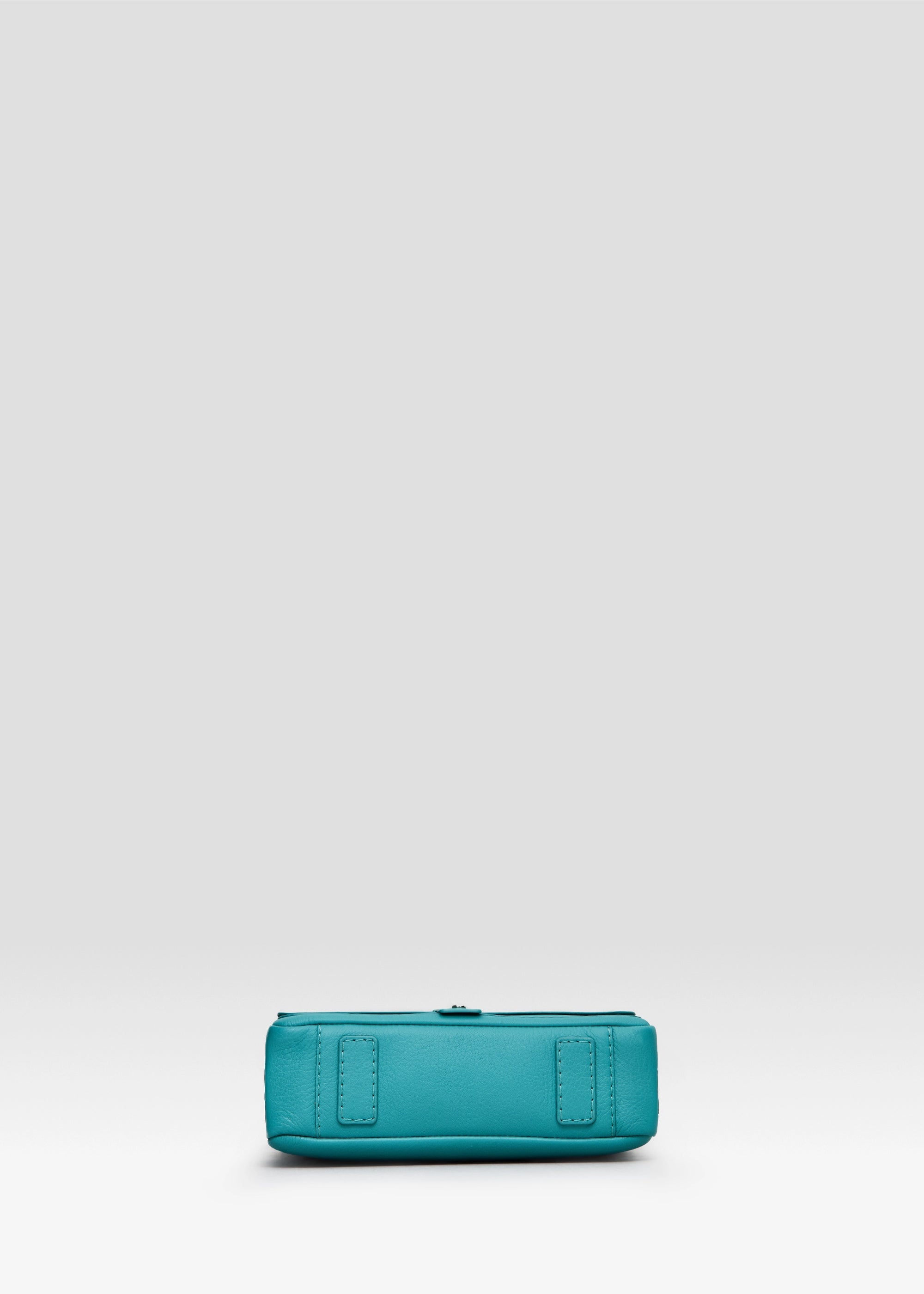 Bottom view of the Philini Whitney Mini Crossbody Bag in turquoise Nappa leather, showcasing the vertical rectangle shape, adjustable leather strap with silver hardware, and secure strap attachment. A handcrafted mini bag is a luxury leather crossbody.