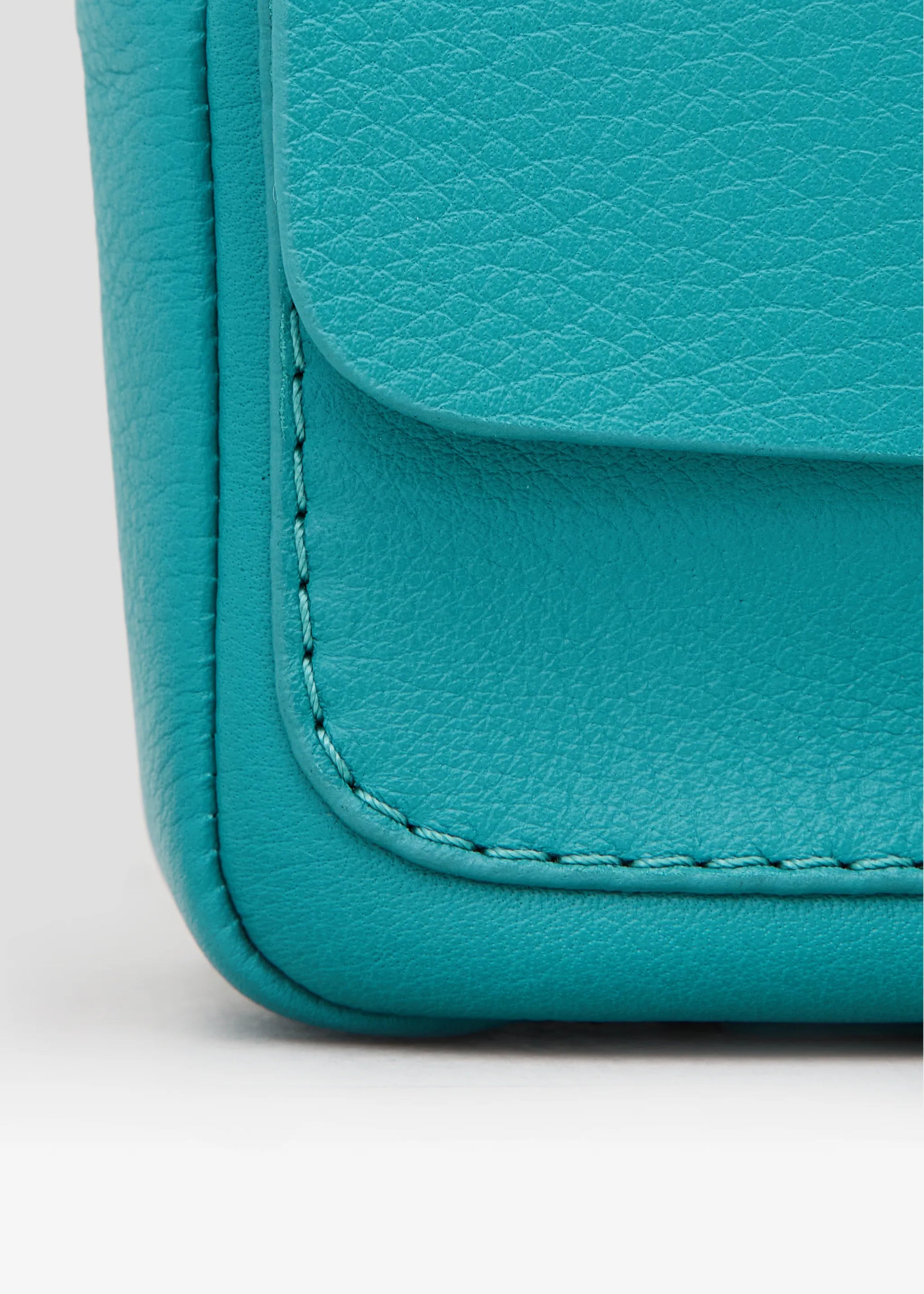Close-up front view of the Philini Whitney Mini Crossbody Bag in turquoise nappa leather, featuring a vertical rectangular shape, silver cufflink closure, adjustable leather strap, and leather bottom pads. A high-quality  mini crossbody for everyday elegant and sustainable style