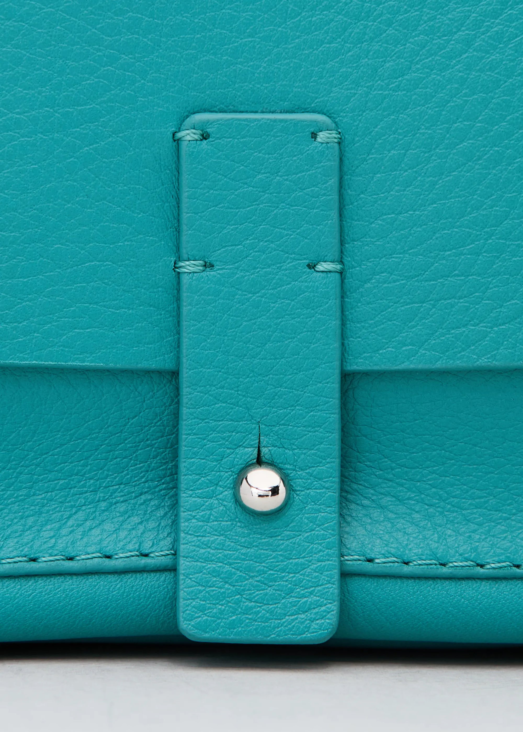 Close front view of the Philini Whitney Mini Crossbody Bag in turquoise nappa leather with silver cufflink closure and adjustable strap. A handcrafted mini designer handbag for elegant, everyday style