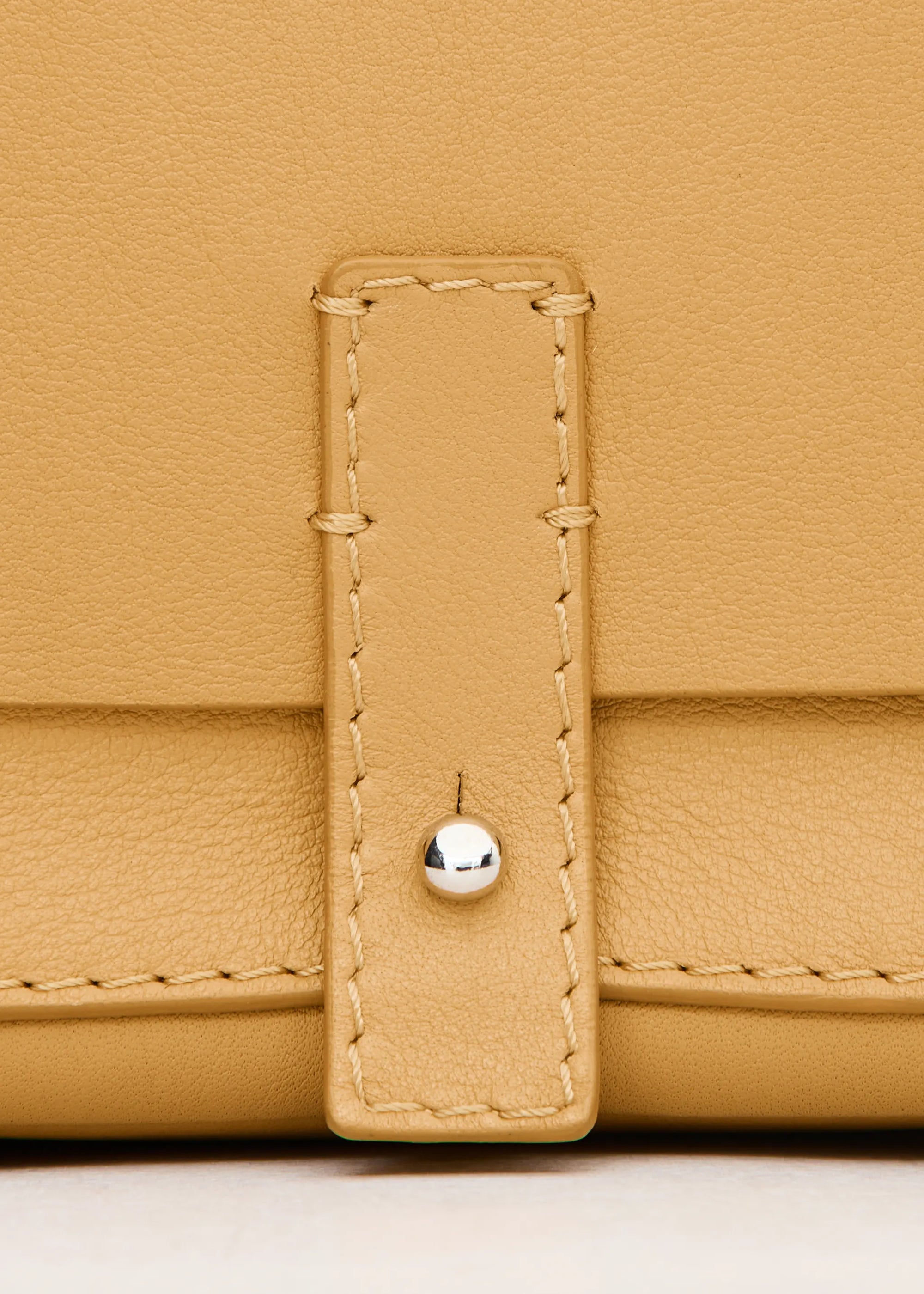 Close front view of the Philini Whitney Mini Crossbody Bag in yellow nappa leather, highlighting its vertical rectangular shape, front flap with silver cufflink closure, and adjustable leather strap with silver hardware. With the addition hand stitches