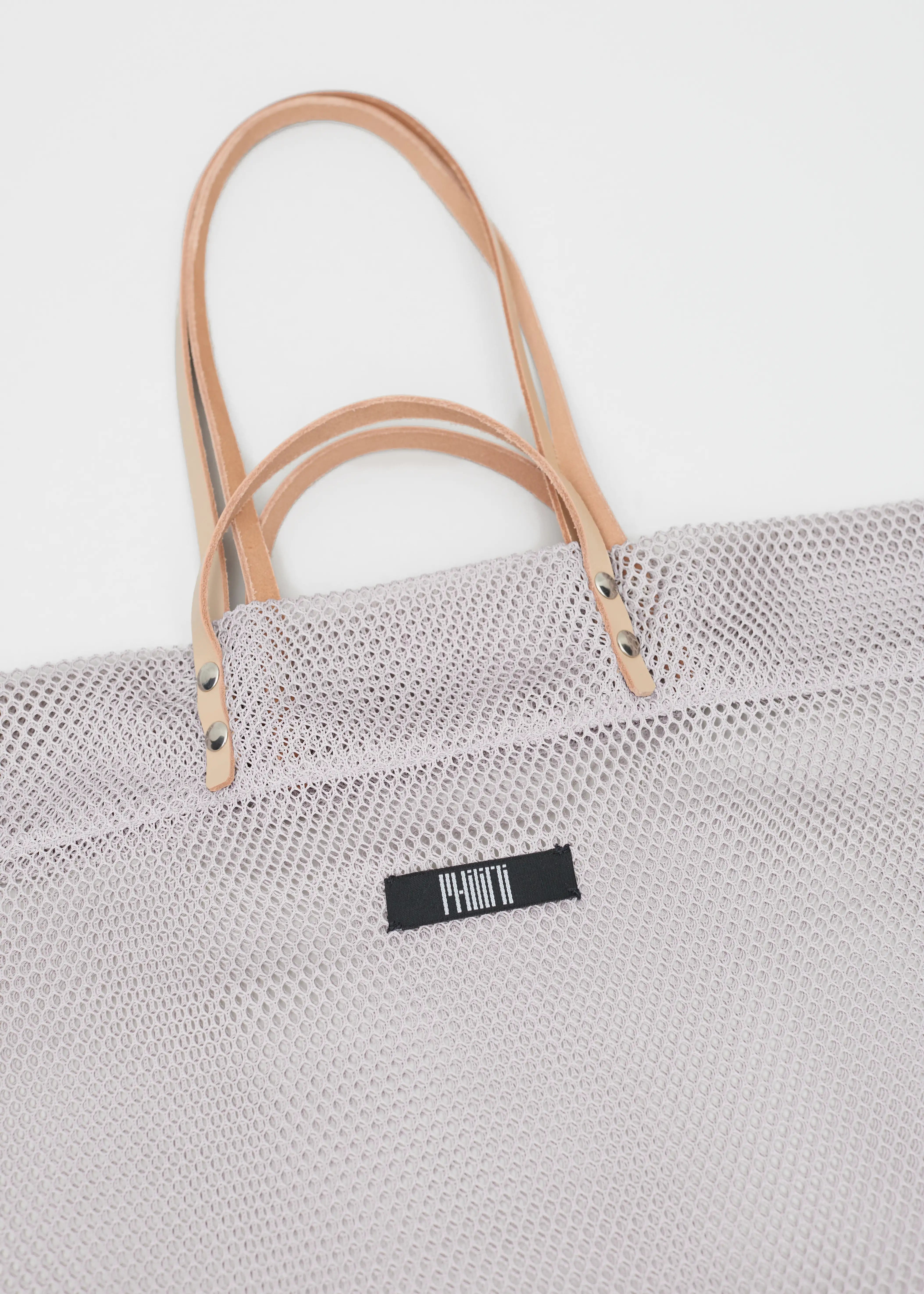 Close-up of the Philini Mesh Shopper, showing both pairs of smooth calf leather handles with silver hardware, crafted in sheer mesh fabric. Lightweight, stylish, and elegant shopper.